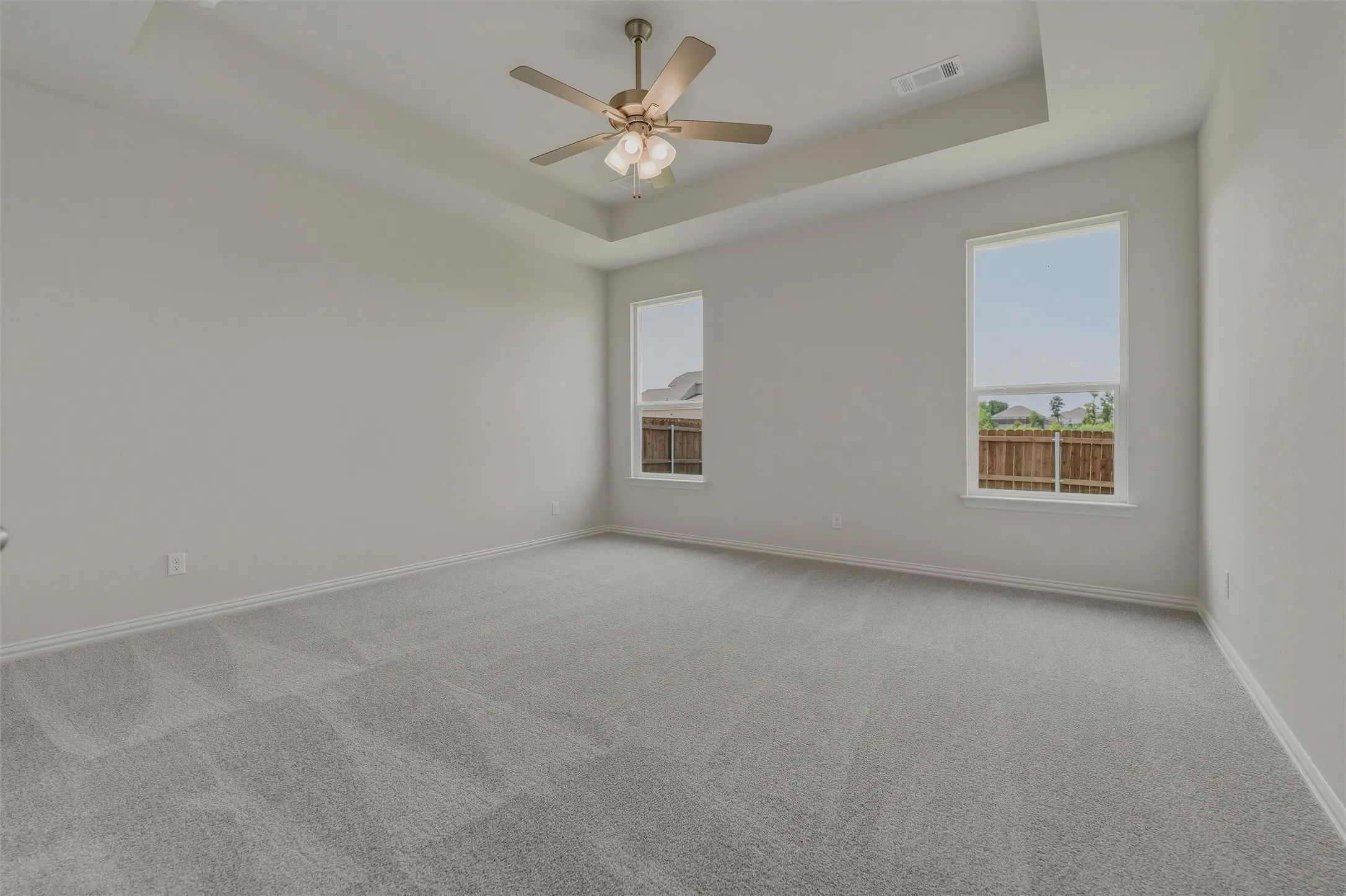 Spacious room featuring a tray ceiling, ceiling fan, two large windows, and wall-to-wall carpeting