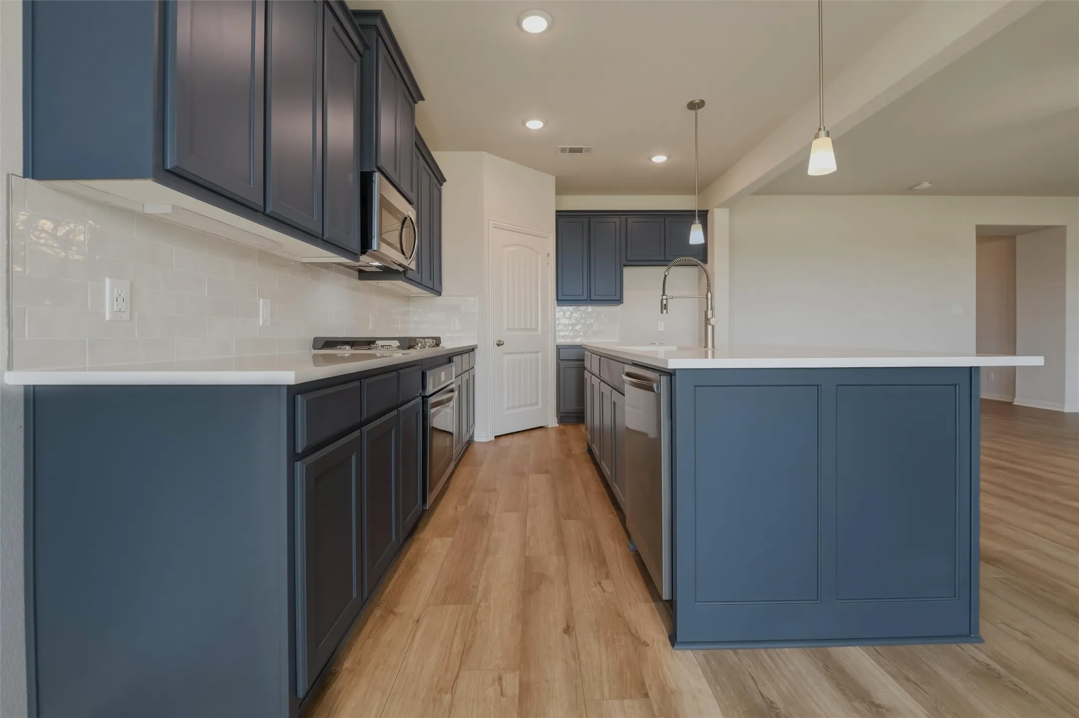 Kitchen featuring wood-finish flooring, dark blue cabinetry, light countertops, subway tile backsplash, and stainless steel appliances