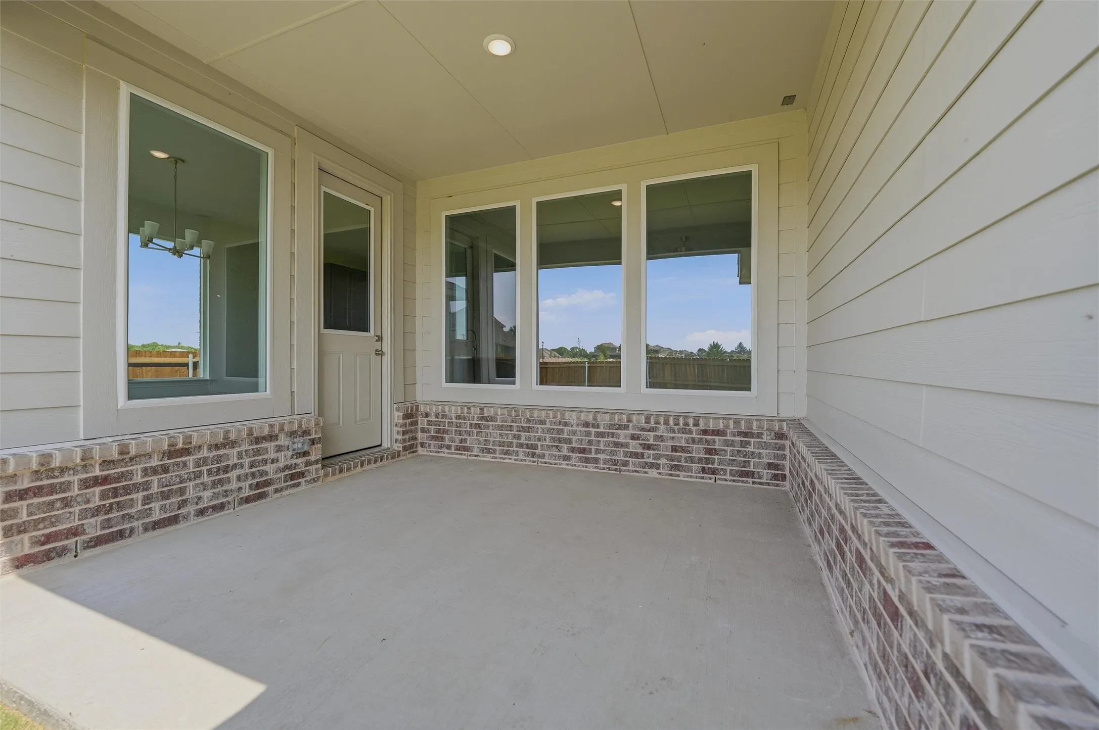 Covered patio featuring a concrete surface, brick wainscoting, a single entry door, and multiple windows