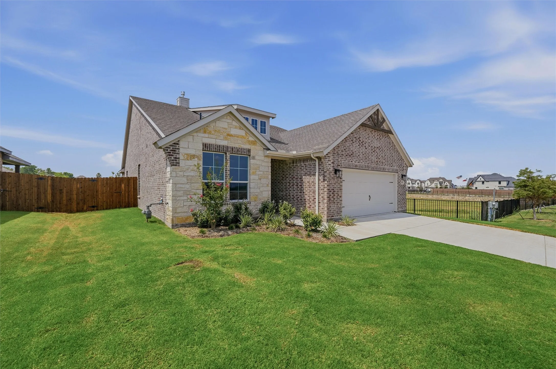 Brick exterior with stone accents, attached garage, concrete driveway, and a wood privacy fence