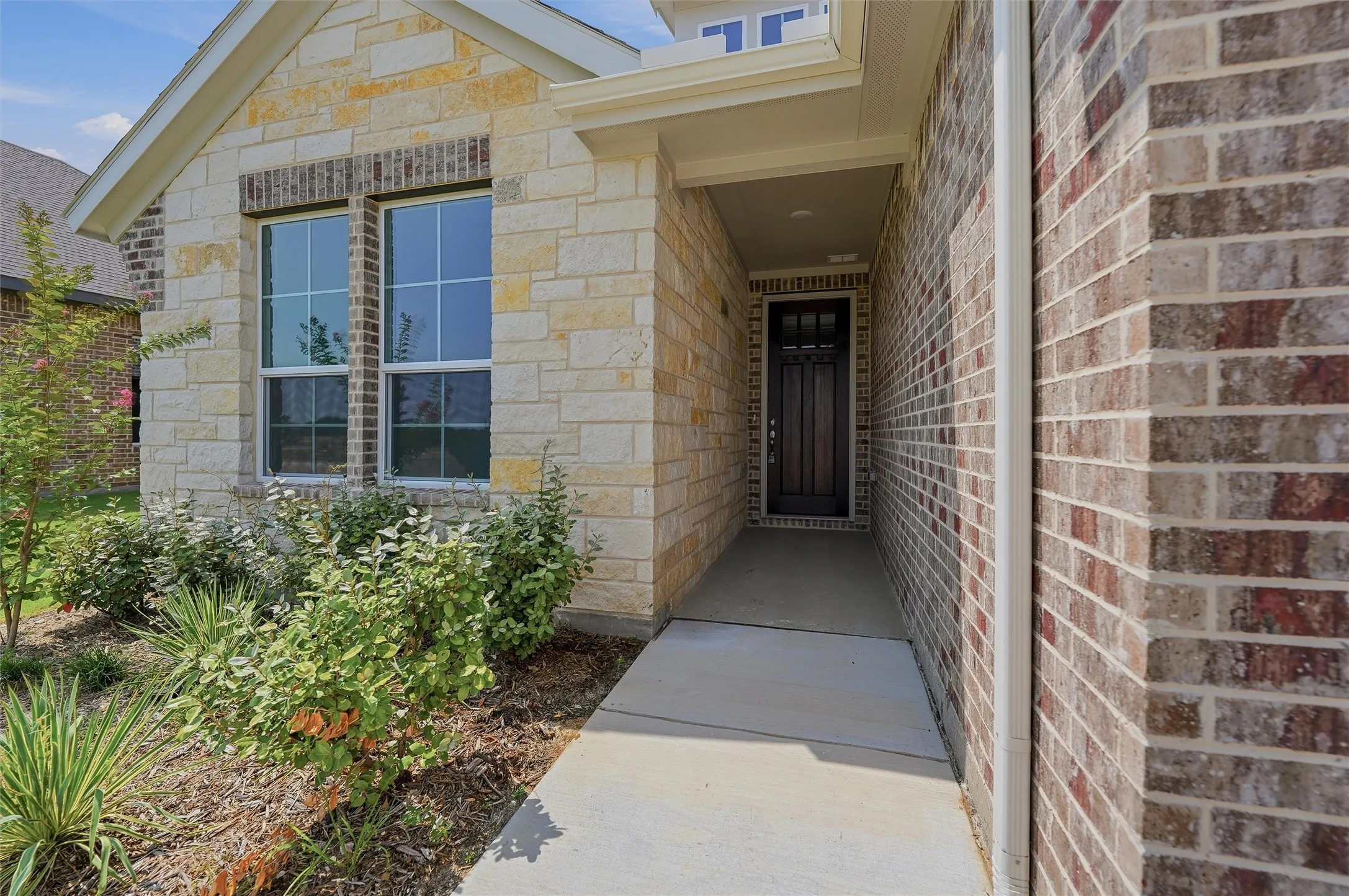 Stone and brick exterior with a covered entry, dark wood-finish front door, and established landscaping