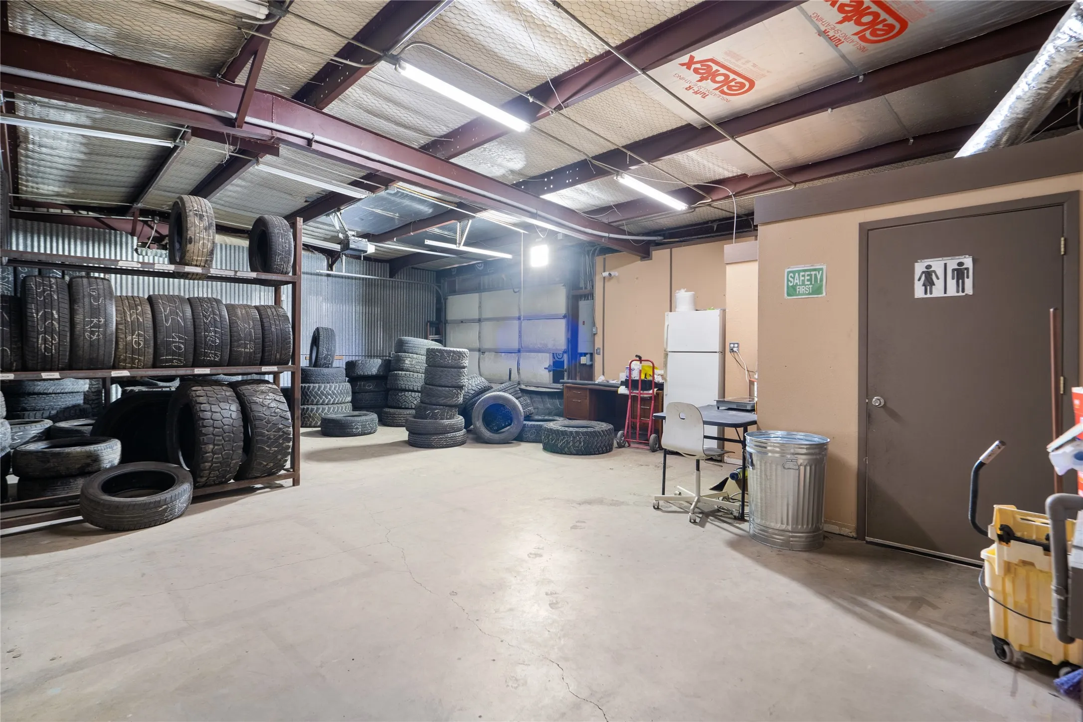 Spacious commercial interior featuring concrete flooring, exposed metal beam construction, and fluorescent lighting