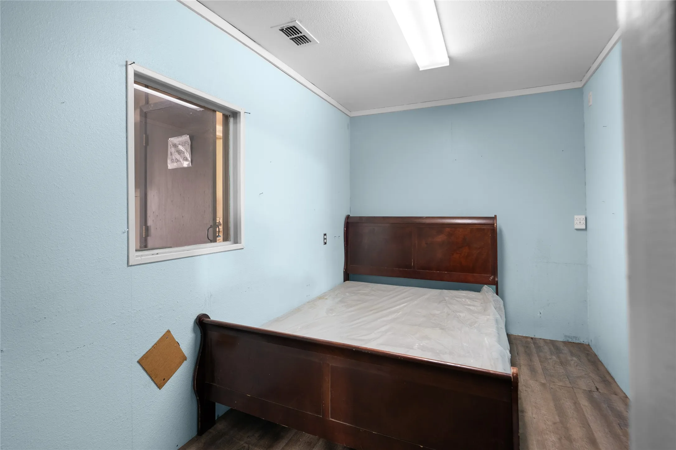 Light blue painted walls with a window, wood-finish flooring, and white ceiling trim