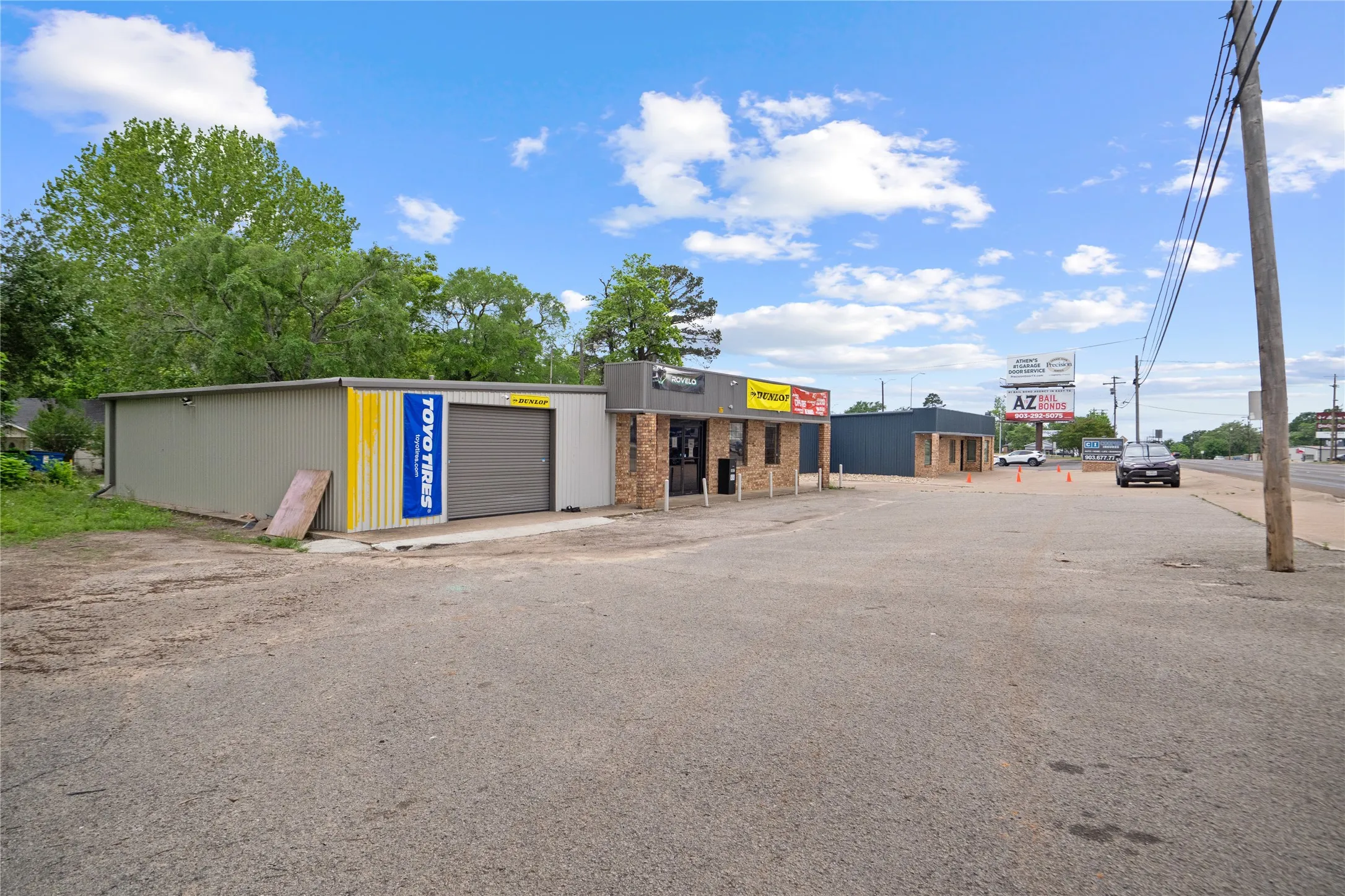 Commercial property featuring multiple structures, including a metal-sided building with a roll-up door, a brick-front building with a storefront, and an additional dark-sided structure