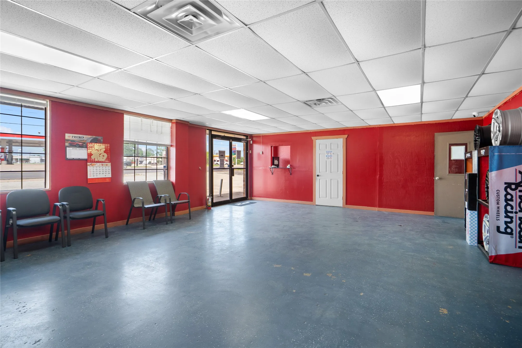 Spacious commercial interior featuring a suspended acoustical tile ceiling with integrated lighting, multiple windows, double glass entry doors, and a durable concrete floor