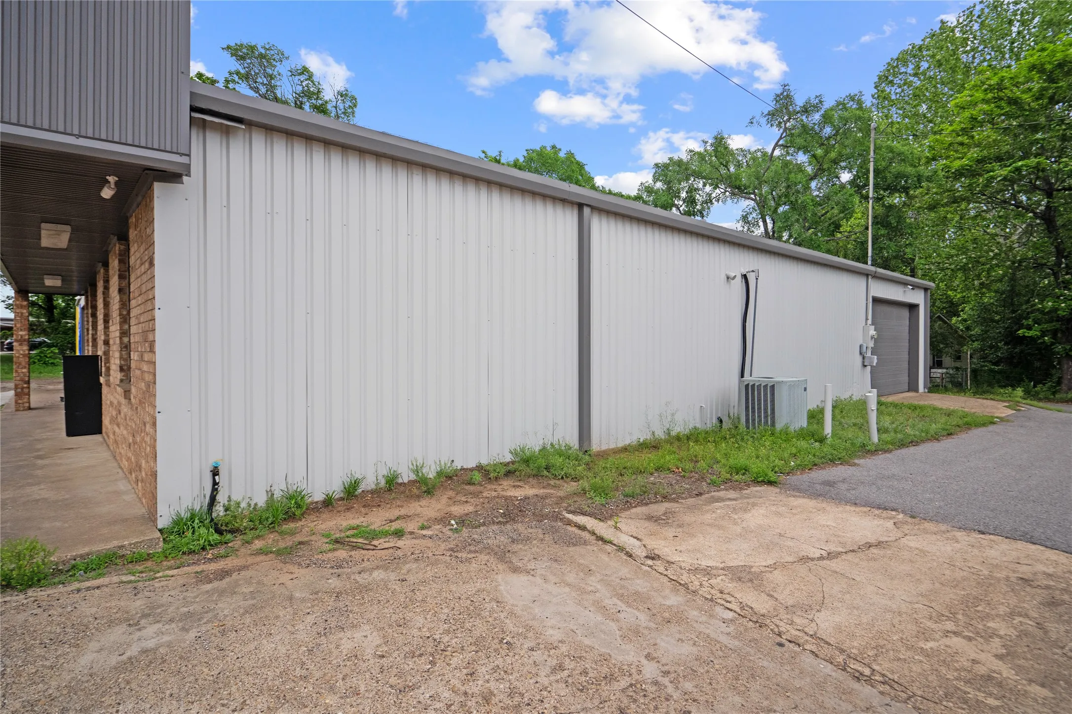 Commercial building featuring a brick facade with a grey metal awning, a metal roll-up door, and an exterior HVAC unit
