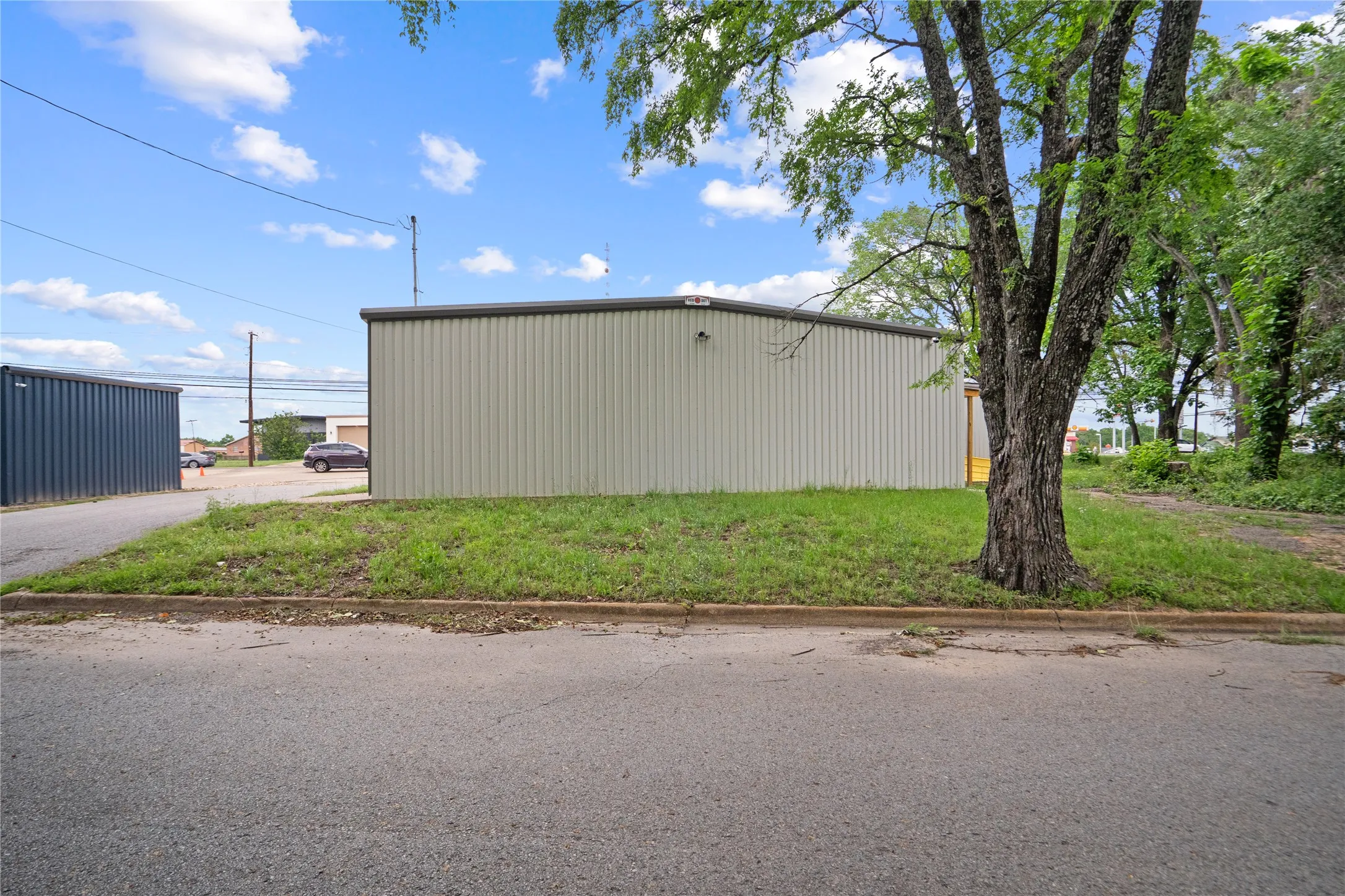 Light-colored corrugated metal building with a dark gray trim, situated on a grassy lot