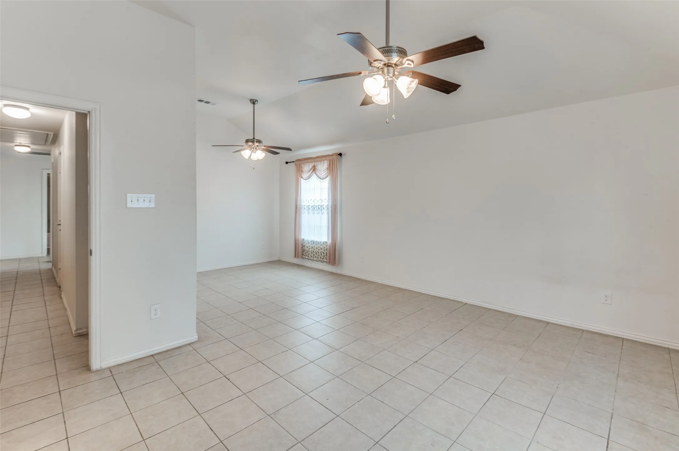 Spacious room featuring tile flooring, vaulted ceiling, and two ceiling fans with integrated lighting