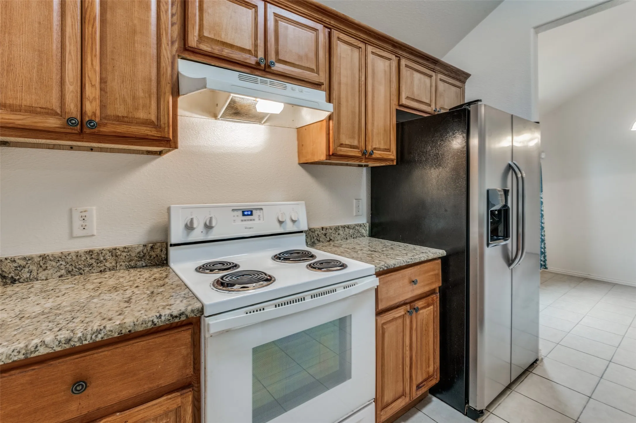 Kitchen featuring a white electric range, wood cabinetry, stone-finish countertops, stainless steel side-by-side refrigerator, and tile flooring