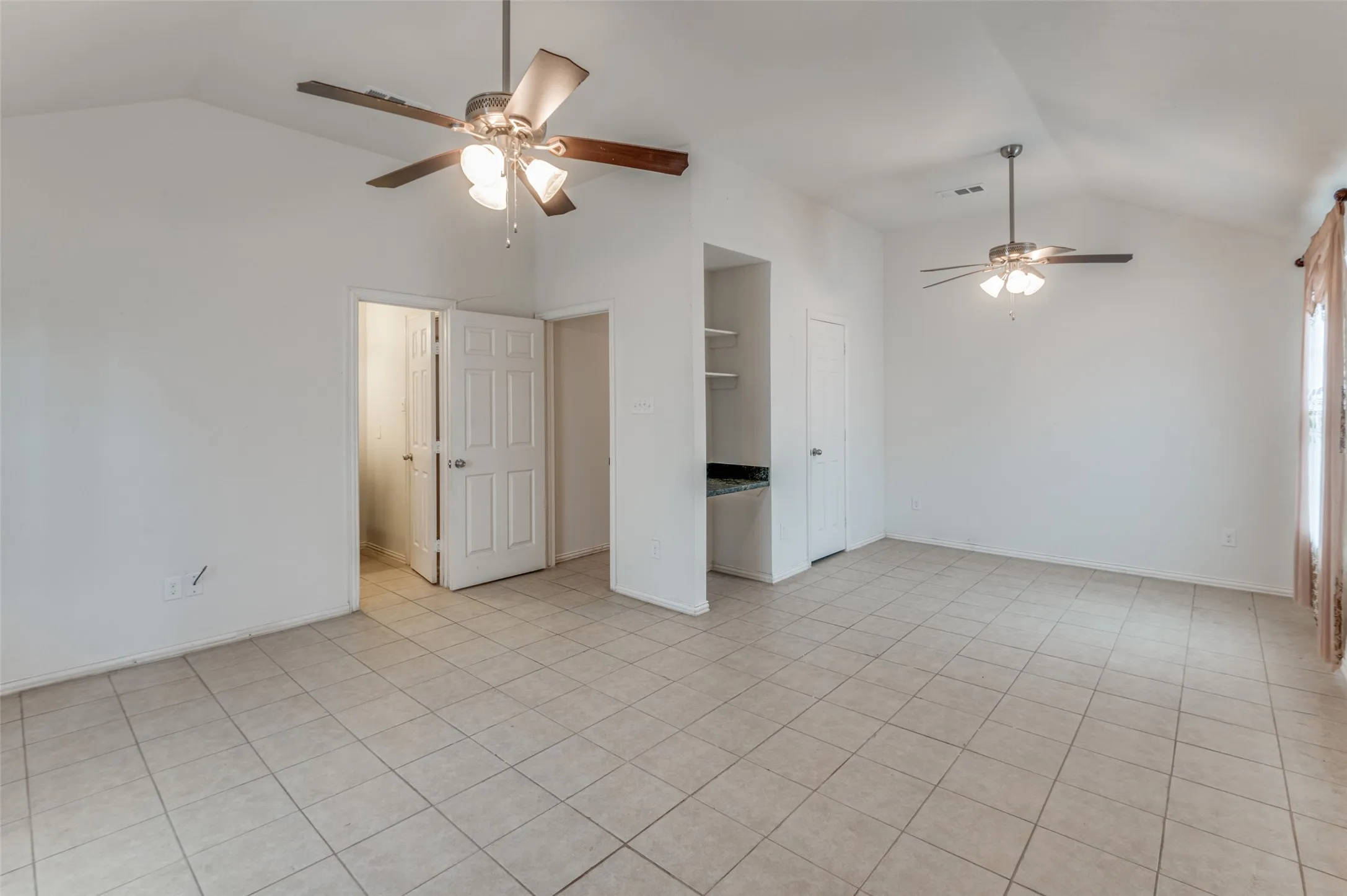 Expansive interior space featuring vaulted ceilings, light-colored tile flooring, and multiple ceiling fans