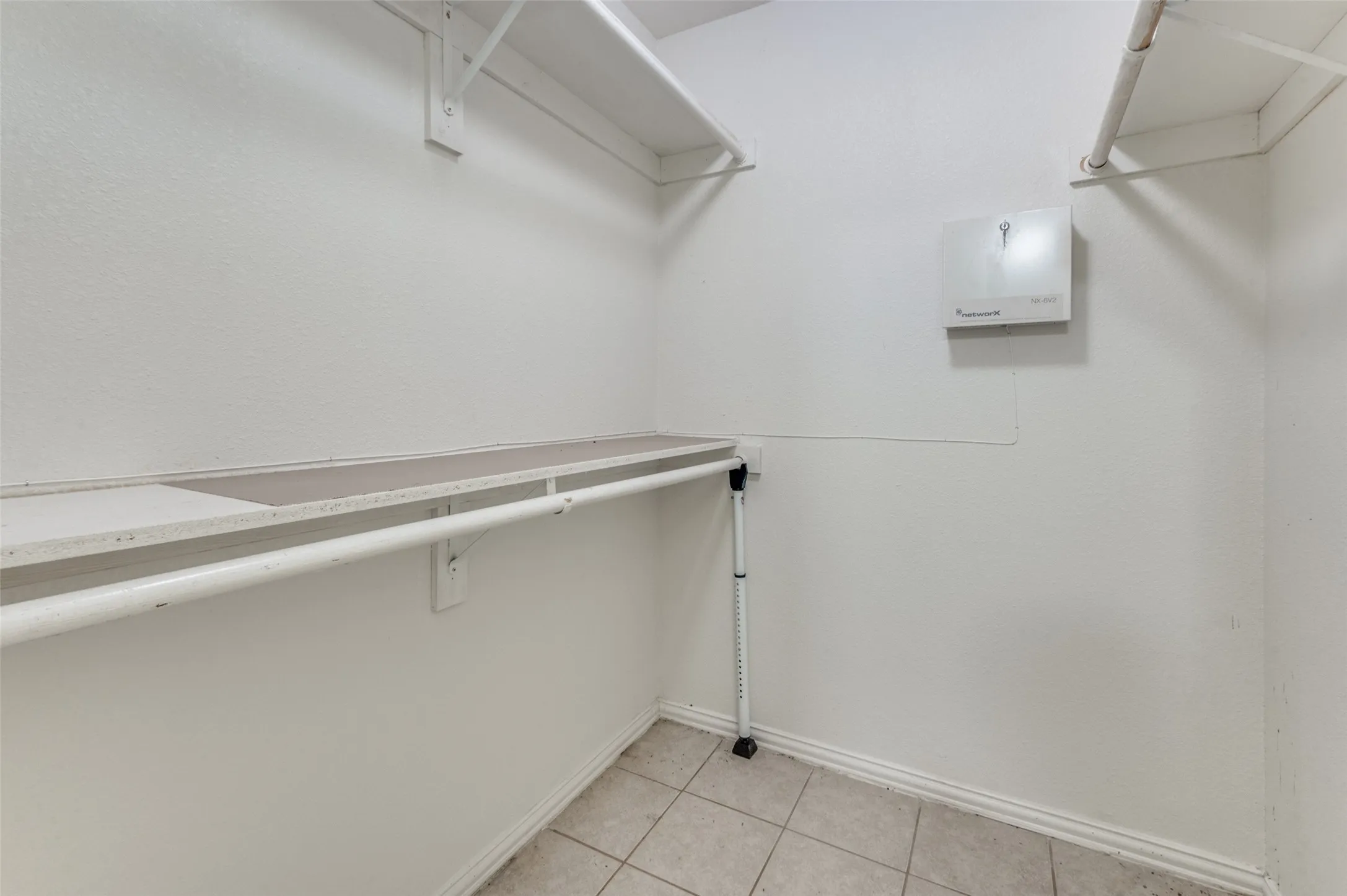 White-painted closet featuring upper and lower shelving, a clothing rod, and tile flooring