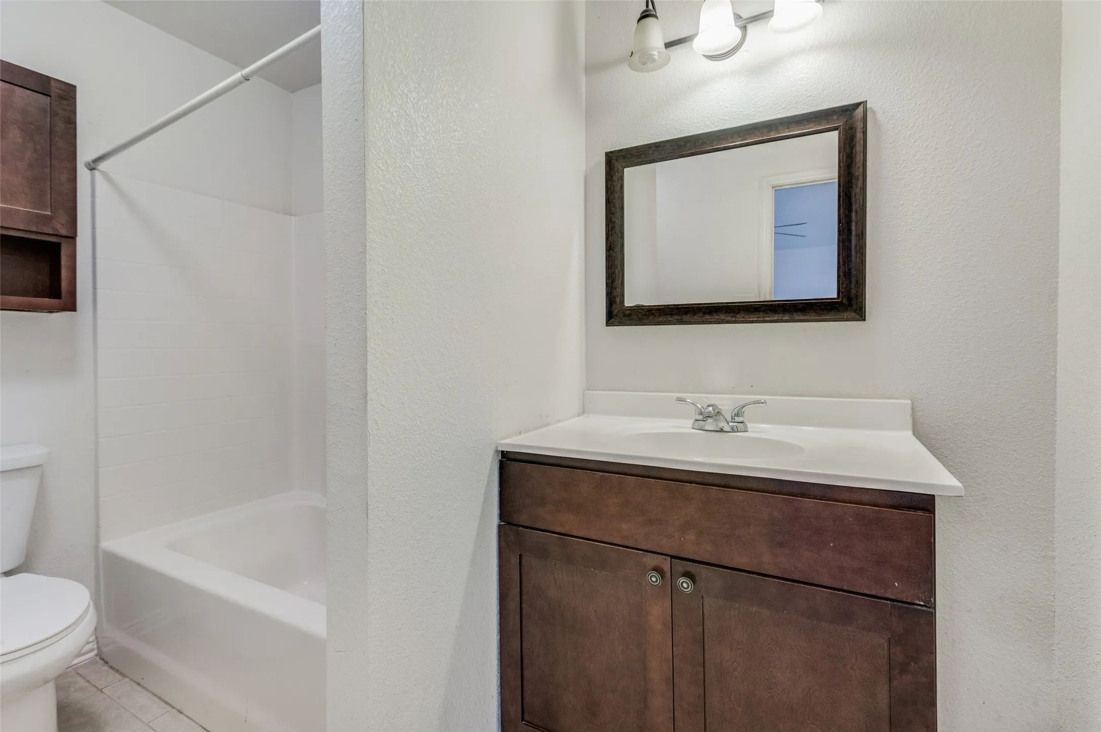 Bathroom featuring a wood-finish vanity with an integrated sink, framed mirror, and a full bathtub with a shower surround