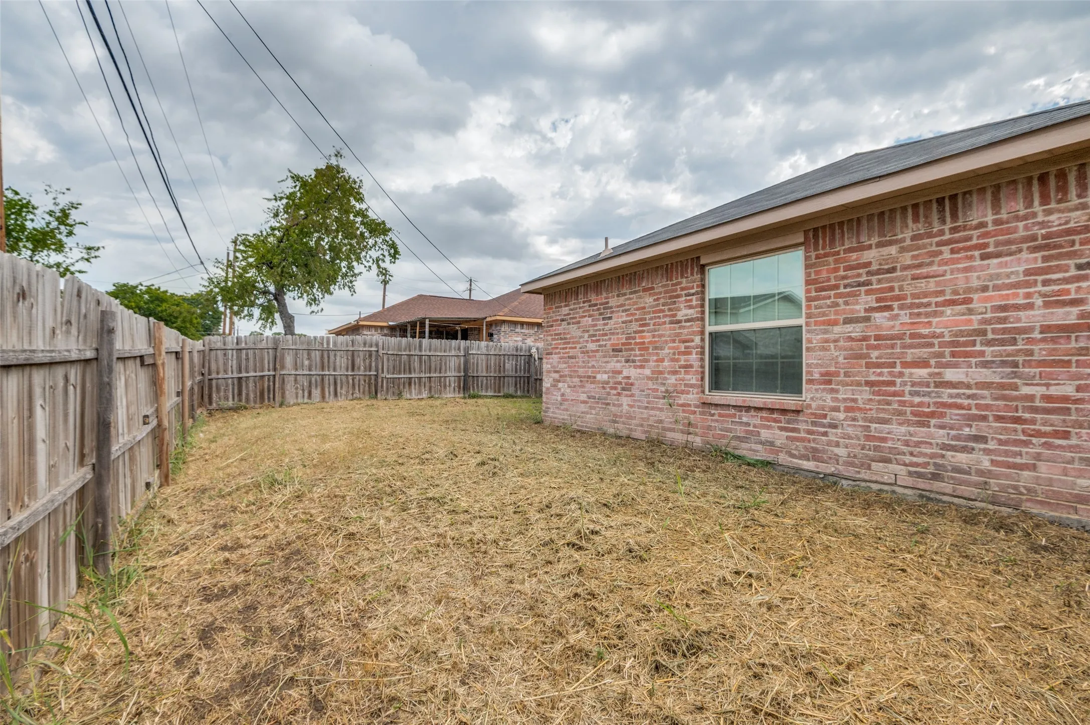Enclosed backyard featuring wood privacy fencing and a brick exterior with a single-pane window