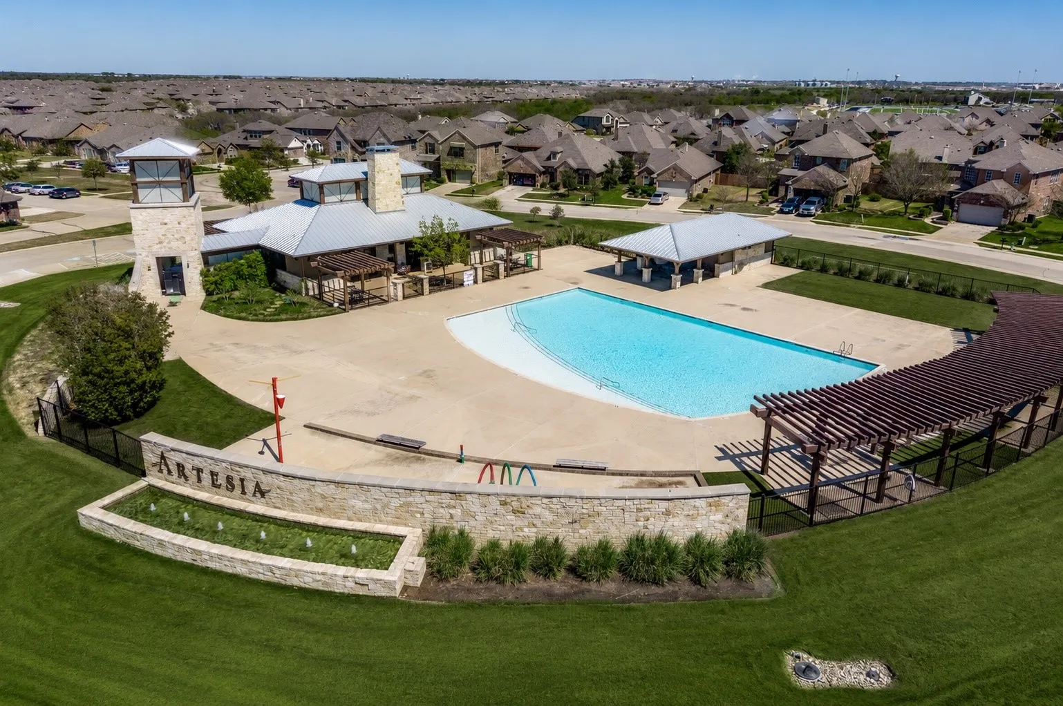 Community amenity center featuring a large swimming pool, stone clubhouse with a metal roof, and an expansive wooden pergola