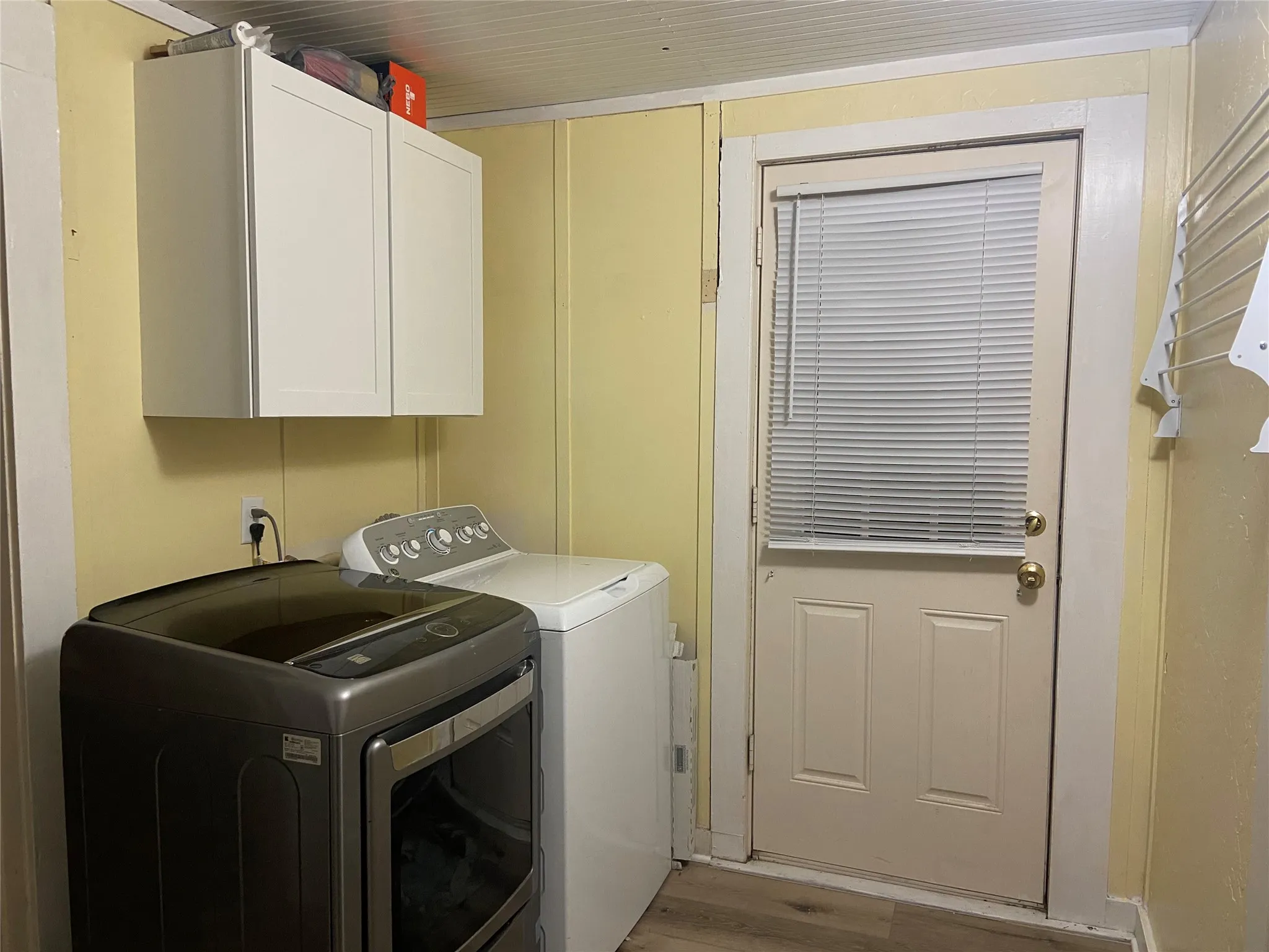 Dedicated laundry area featuring overhead cabinetry, panel wall detailing, a paneled door with window blinds, and wood-finish flooring