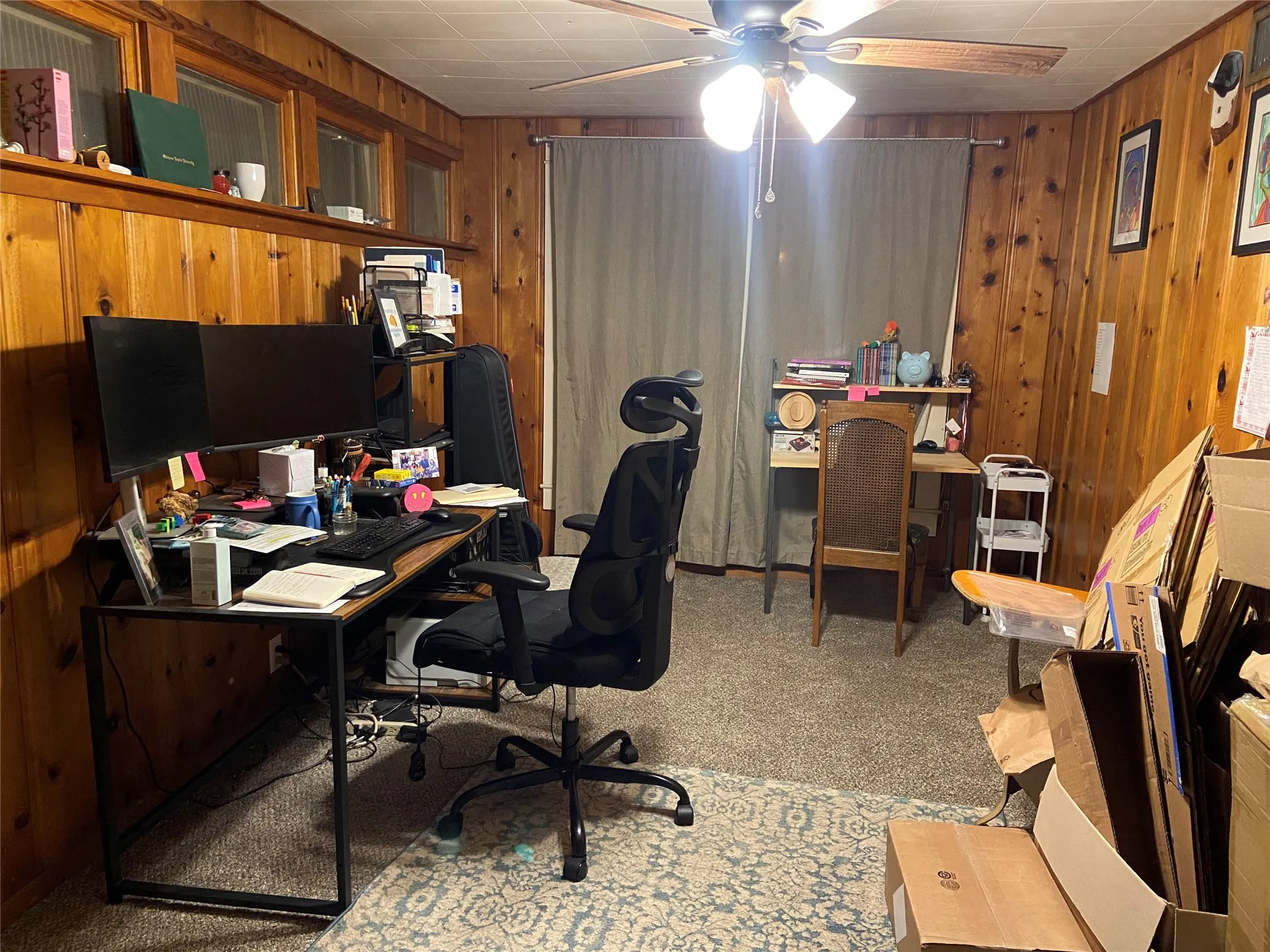 Room featuring wood paneling on walls, carpeted flooring, and a ceiling fan with integrated lighting