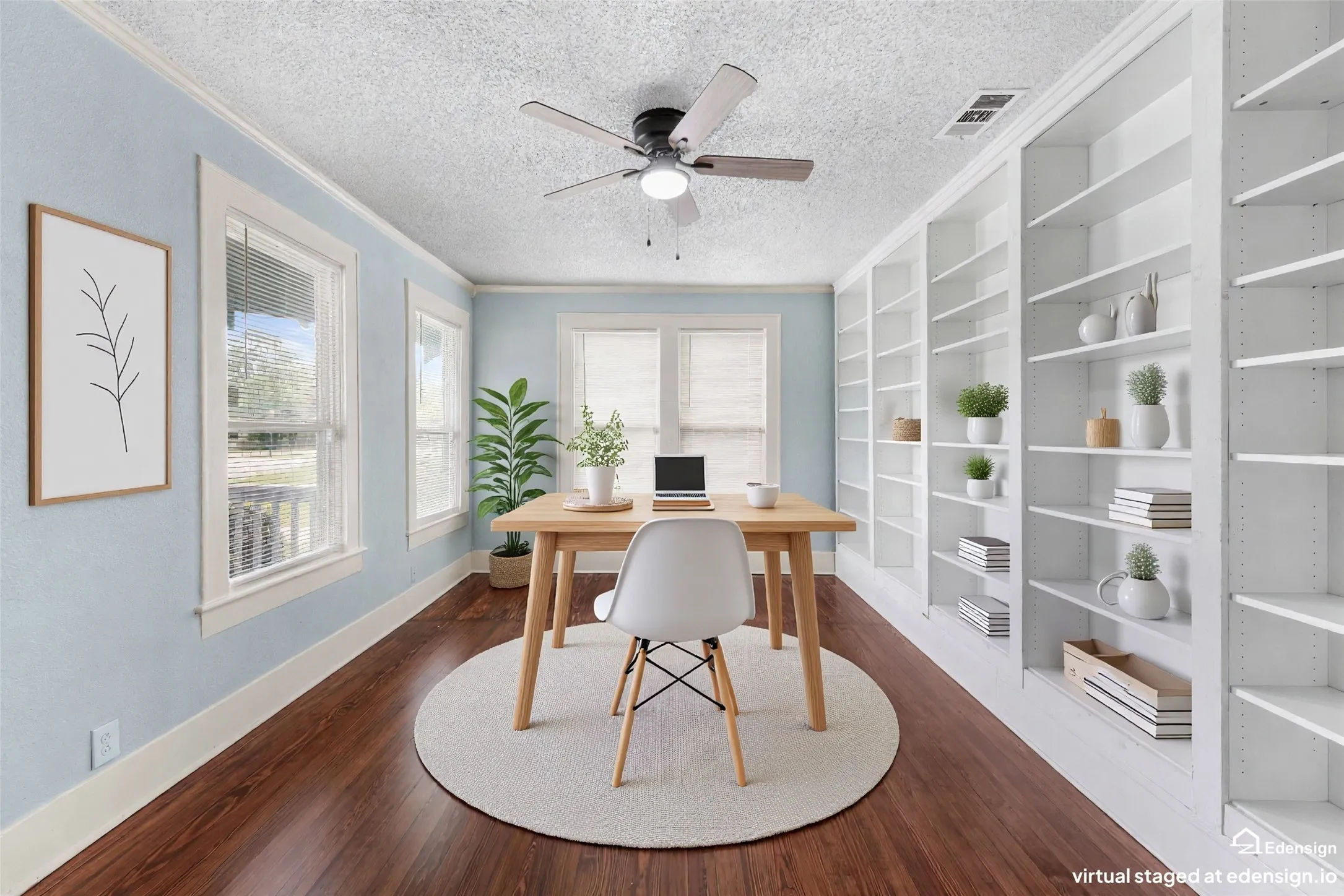 Office space featuring extensive built-in white shelving, wood-finish flooring, multiple windows with white trim, a ceiling fan, and light blue wall tones
