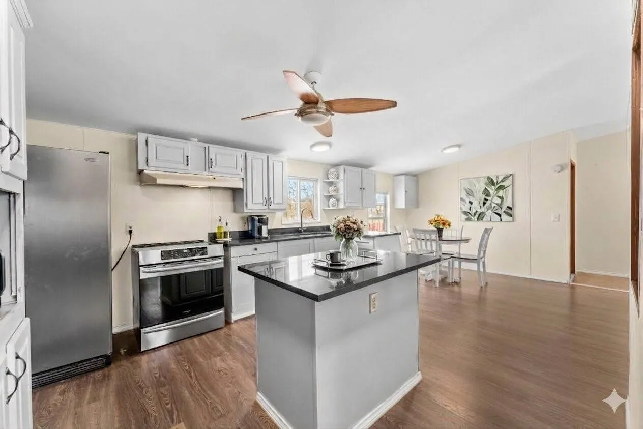 Kitchen featuring wood-finish flooring, light grey cabinetry, stainless steel appliances, a center island with a dark countertop, and a ceiling fan