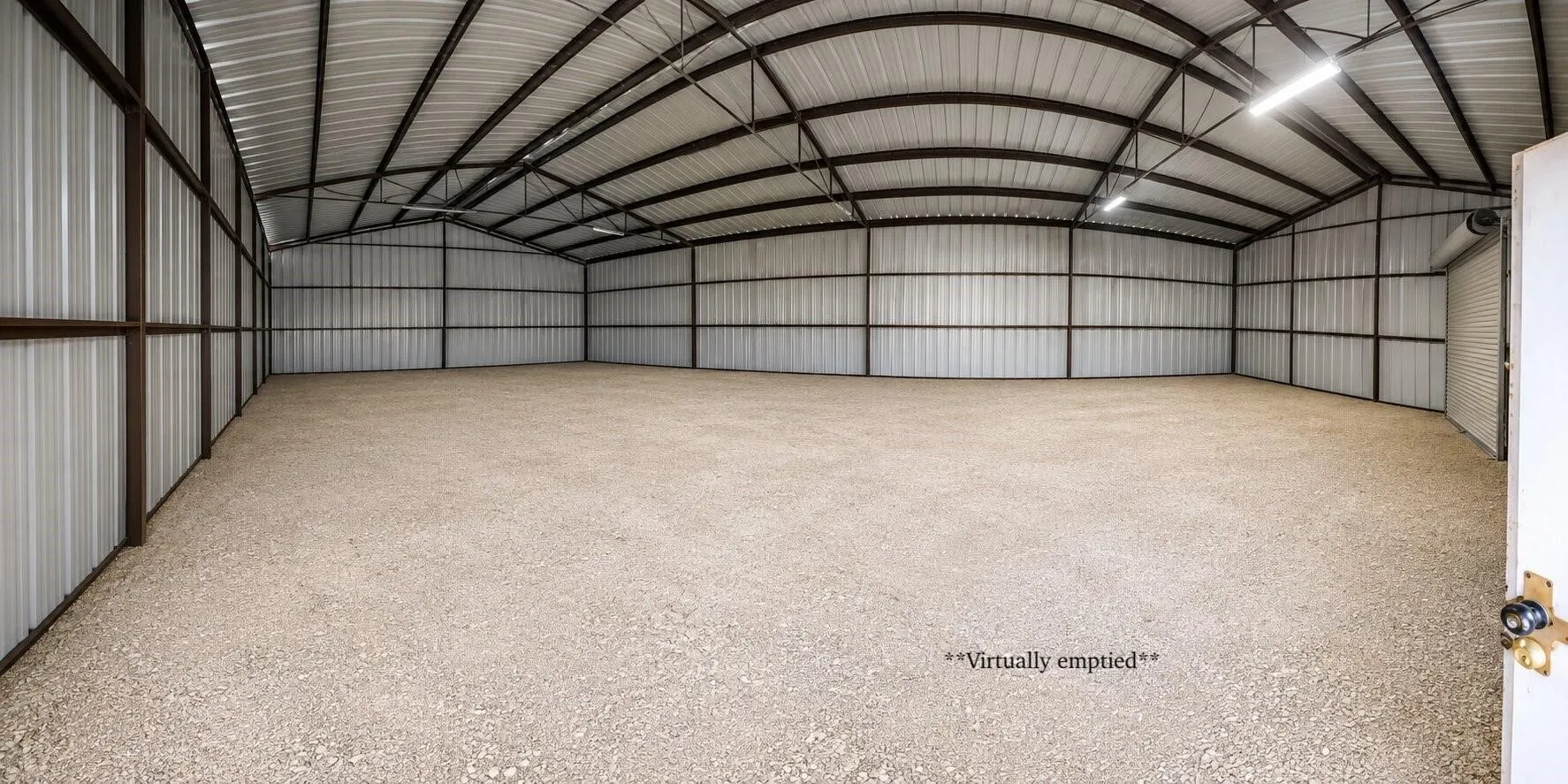 Spacious metal building with a gravel floor, exposed metal truss roof, and integrated ceiling lighting