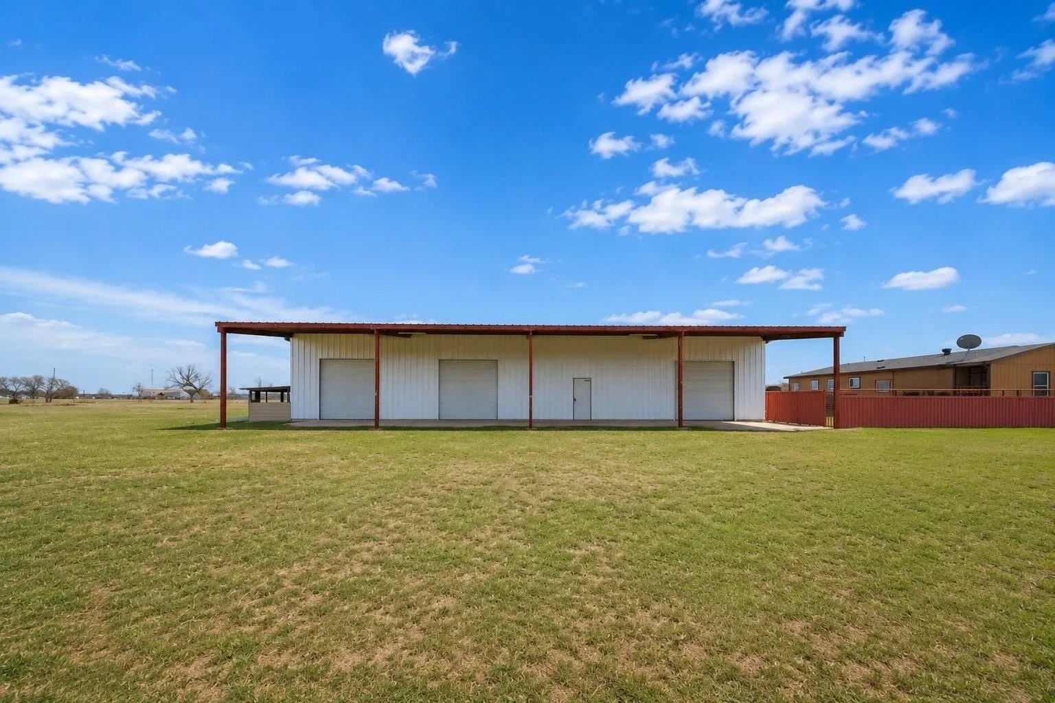 Expansive open field with a large metal building featuring a covered entryway, multiple roll-up doors, and a side entry door