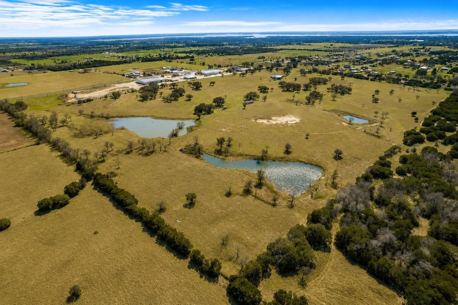 Expansive land featuring three ponds, scattered mature trees, and a distant body of water