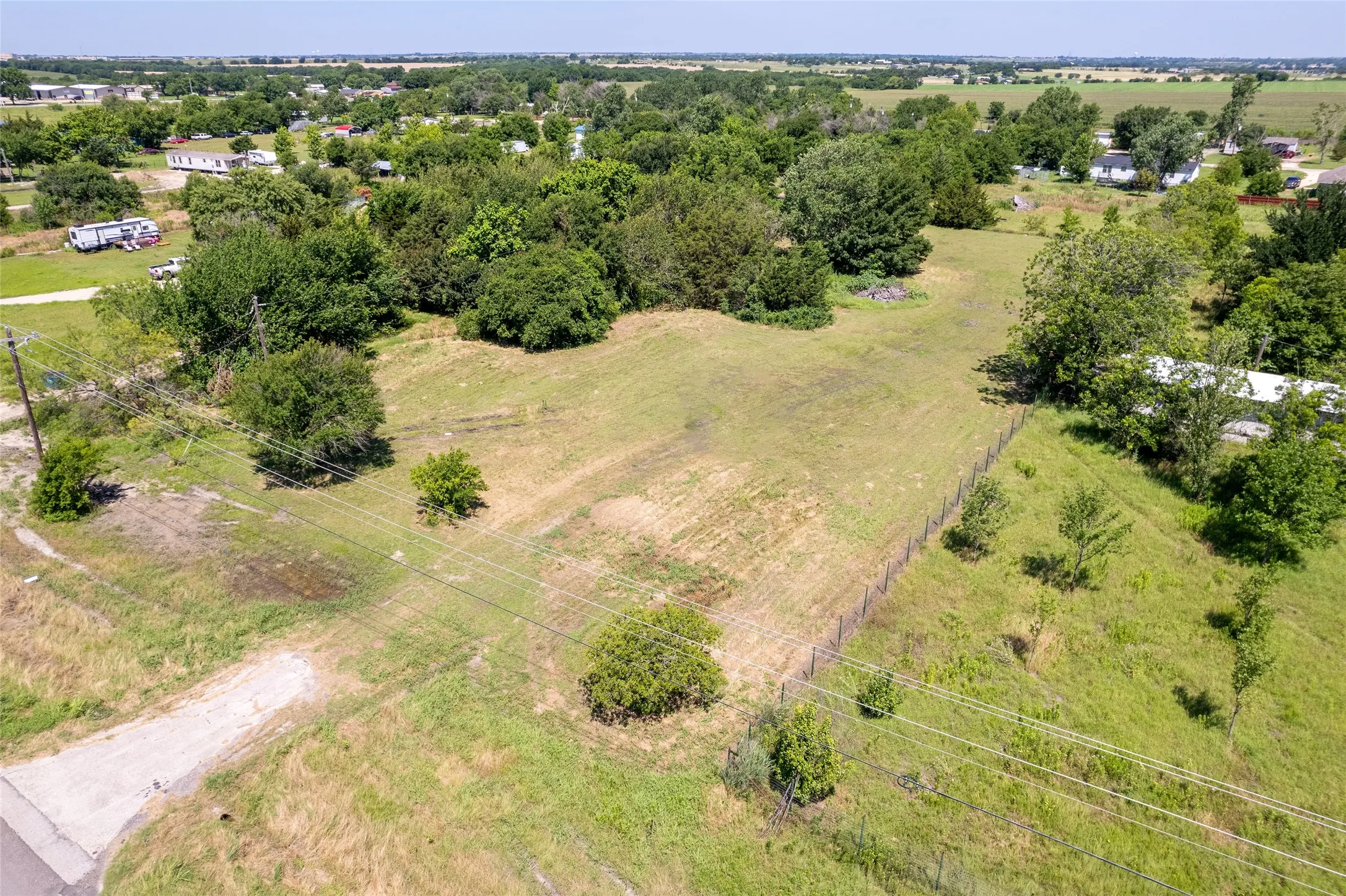Expansive undeveloped parcel featuring open land, scattered mature trees, a perimeter fence, and visible utility lines