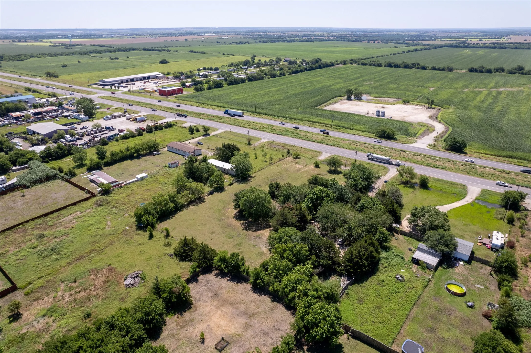 Expansive property featuring a highway frontage, multiple structures, significant undeveloped land, mature trees, and agricultural fields in the background