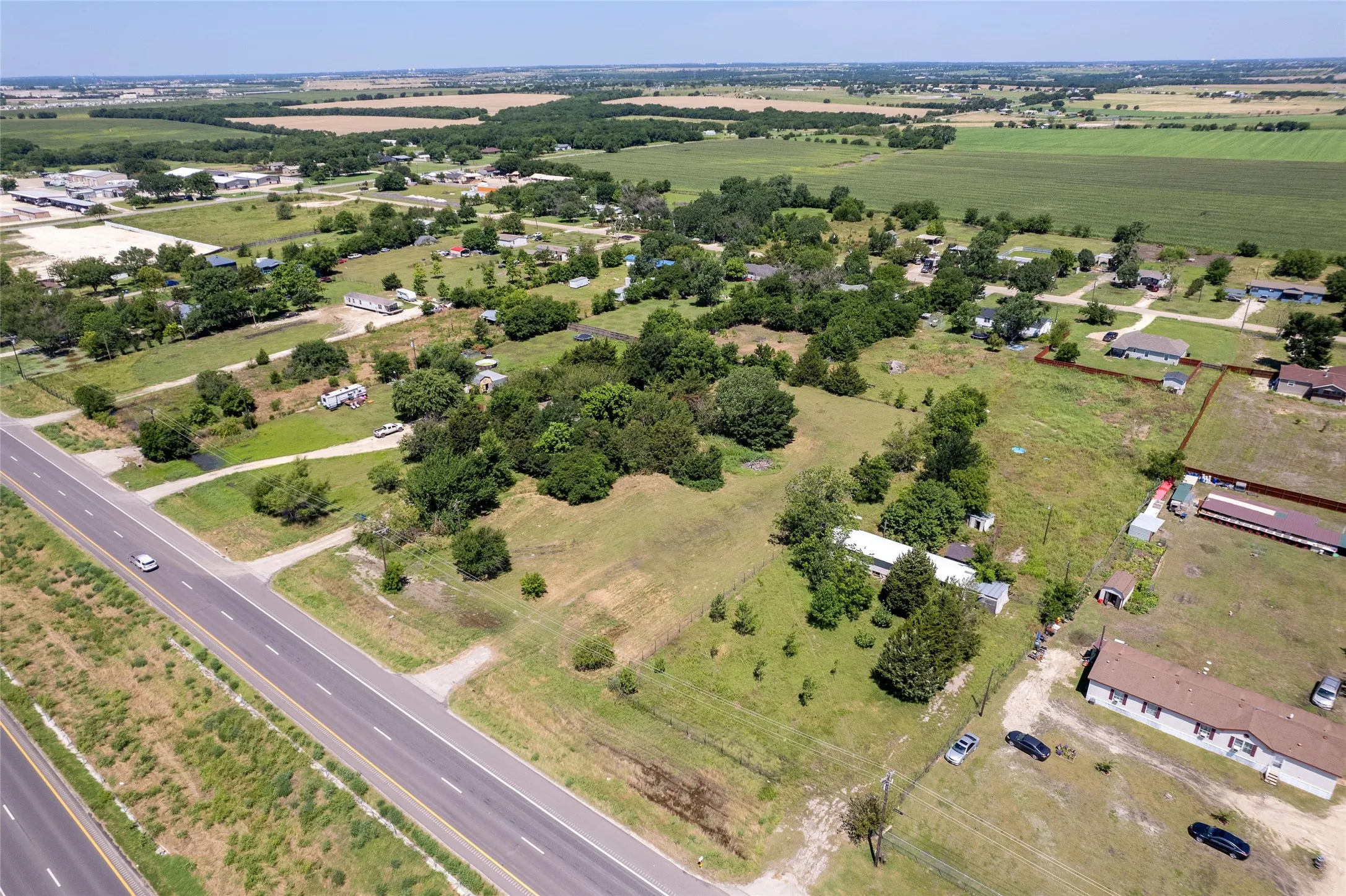 Expansive rural landscape featuring a highway, green fields, scattered trees, and residential structures