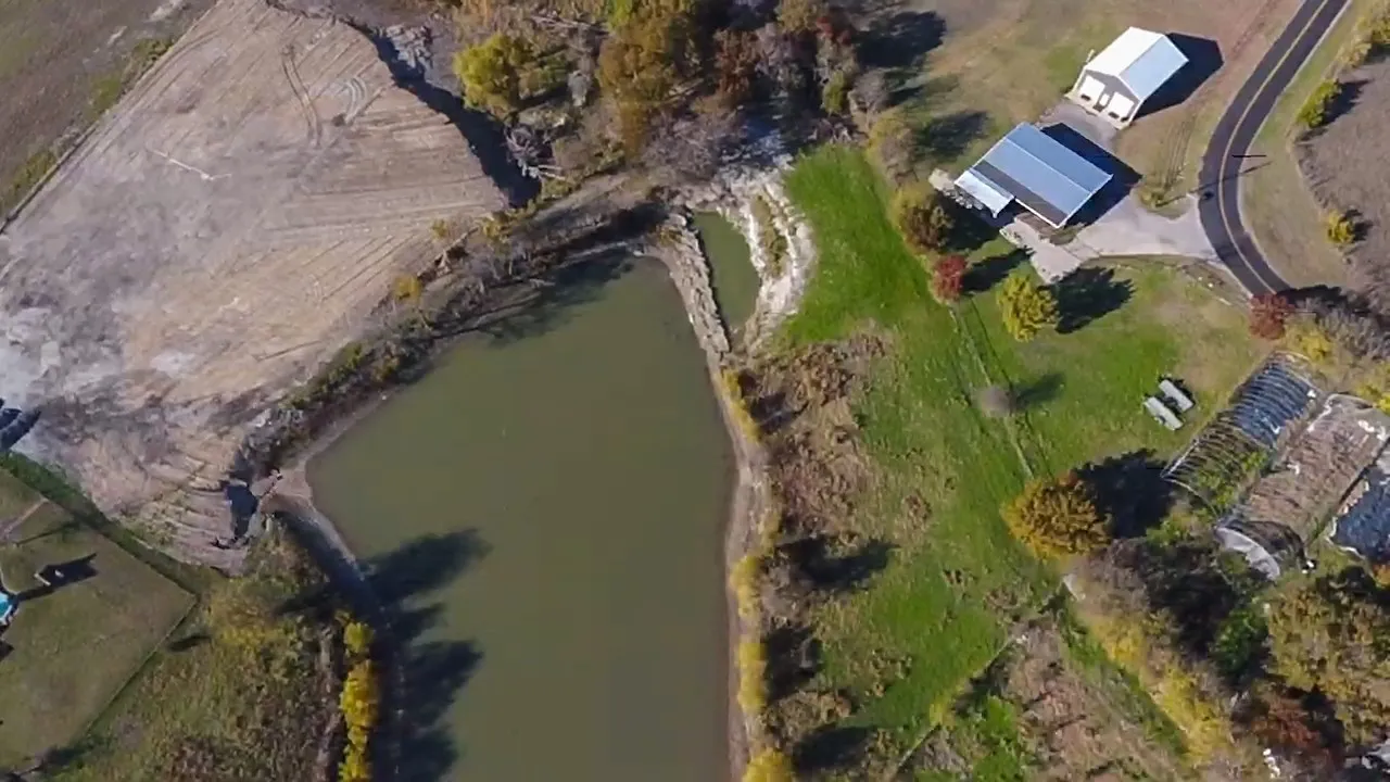 Expansive property featuring a large pond, agricultural fields, multiple outbuildings, a paved driveway, and mature landscaping