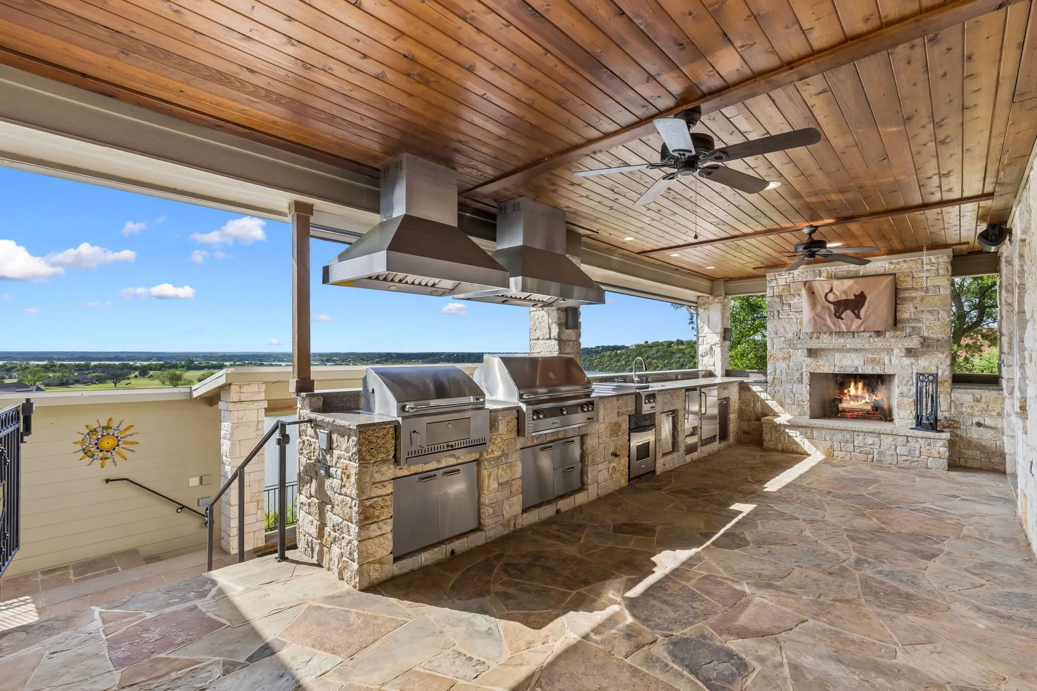 Outdoor kitchen and living area featuring a fantastic stone fireplace with TV, outdoor oven, and two grills—perfect for keeping the main kitchen cool during hot summer days.