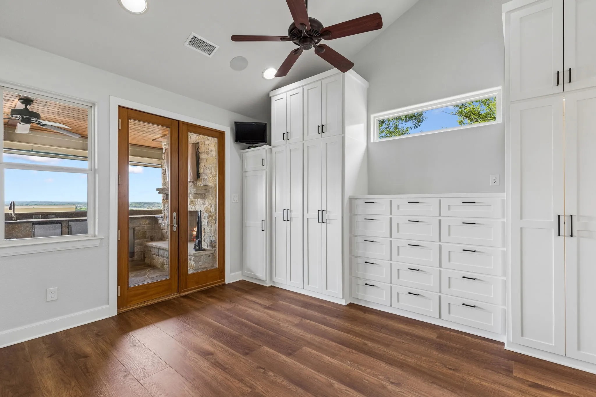 Custom, carpenter-crafted built-in cabinetry lines the primary bedroom, thoughtfully designed with extensive soft close drawers and storage organization, complemented by a full wall of mirror not pictured. The space flows seamlessly into the spacious primary bath and opens to the upper-tier covered terrace adjacent to the outdoor wood-burning fireplace and living area.