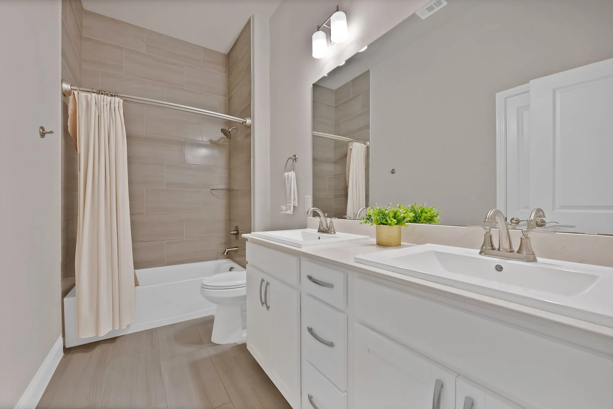Bathroom featuring dual sinks with brush nickel faucets, a vanity with white cabinets, a shower-tub combination with tile surround, and light-colored flooring