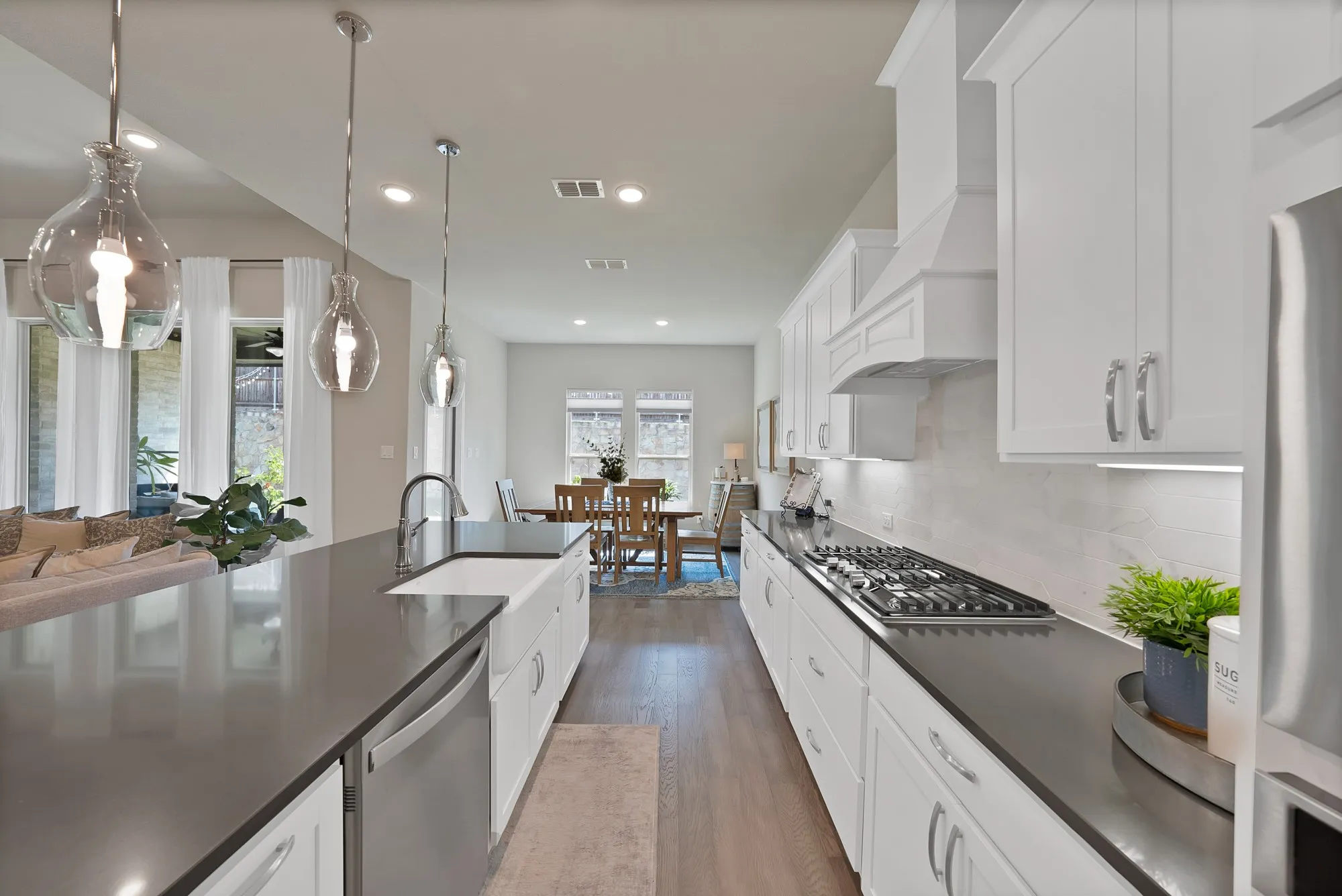 Modern kitchen featuring white cabinetry, dark countertops, a gas range, and a kitchen island with a farmhouse sink and pendant lighting