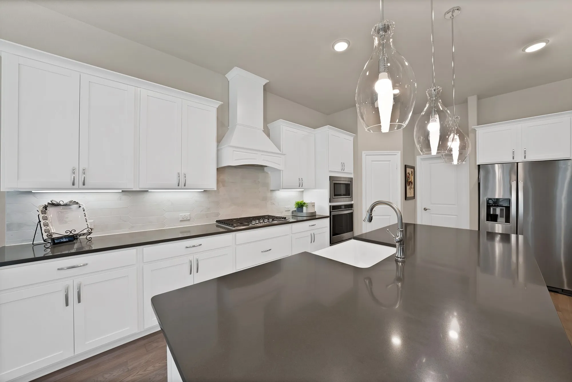 Modern kitchen with white cabinetry, dark countertops, a stainless steel refrigerator, and pendant lighting