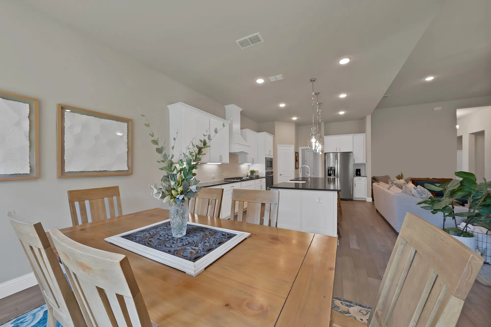 This open concept living area features hardwood style flooring, recessed lighting, and a kitchen with white cabinetry, a central island, and stainless steel appliances