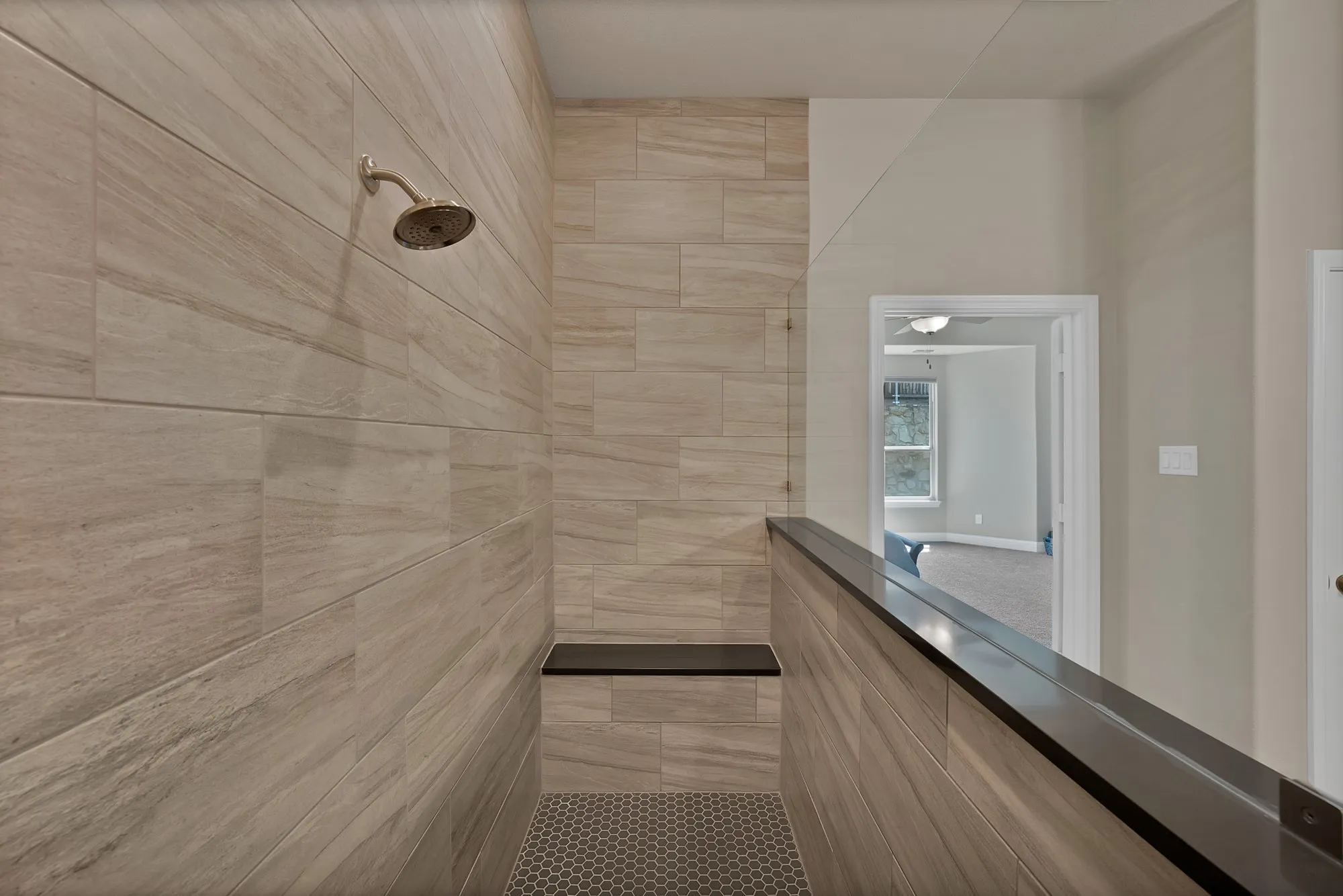 Modern shower with neutral-toned tiled walls, a built-in bench, and a hexagonal tiled floor