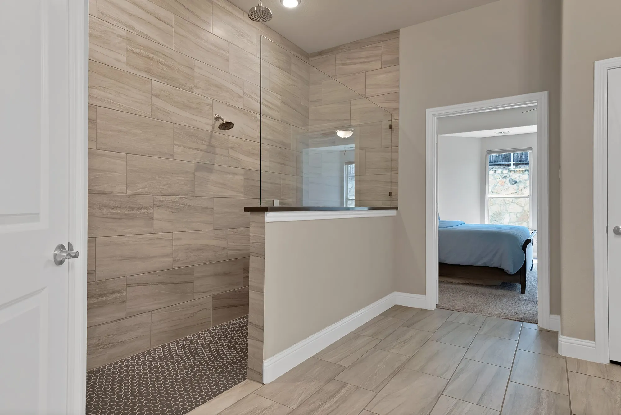 This bathroom features a spacious shower with large format tile walls and a hexagonal tile floor, complete with a glass partition