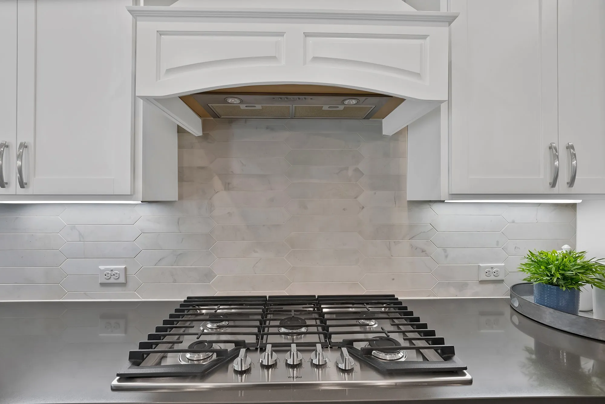 The kitchen features a gas cooktop, a stylish range hood, white cabinetry, and a light-toned backsplash