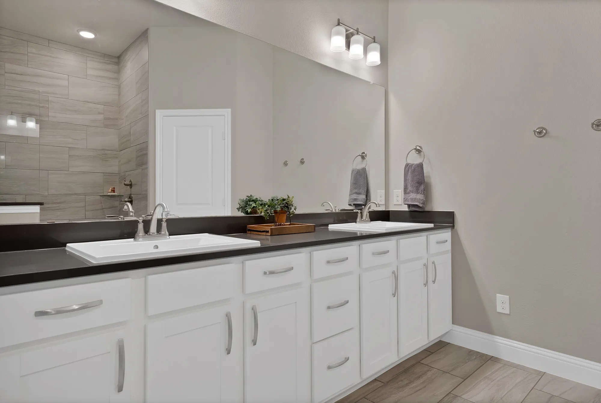 This bathroom features dual sinks with brushed nickel faucets, a spacious vanity with white cabinetry and dark countertops, and a large mirror