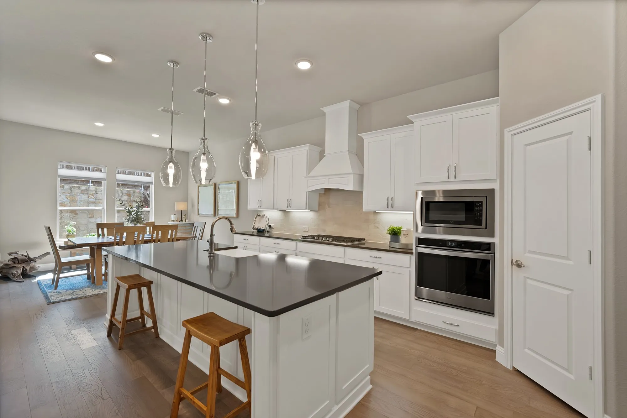 The kitchen features white cabinetry, stainless steel appliances, a dark countertop, and a center island with a sink and pendant lighting