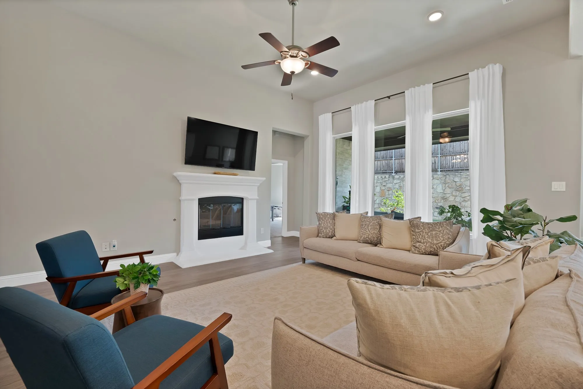 The inviting living area features a fireplace with a white mantel, high ceilings, and large windows with white drapes