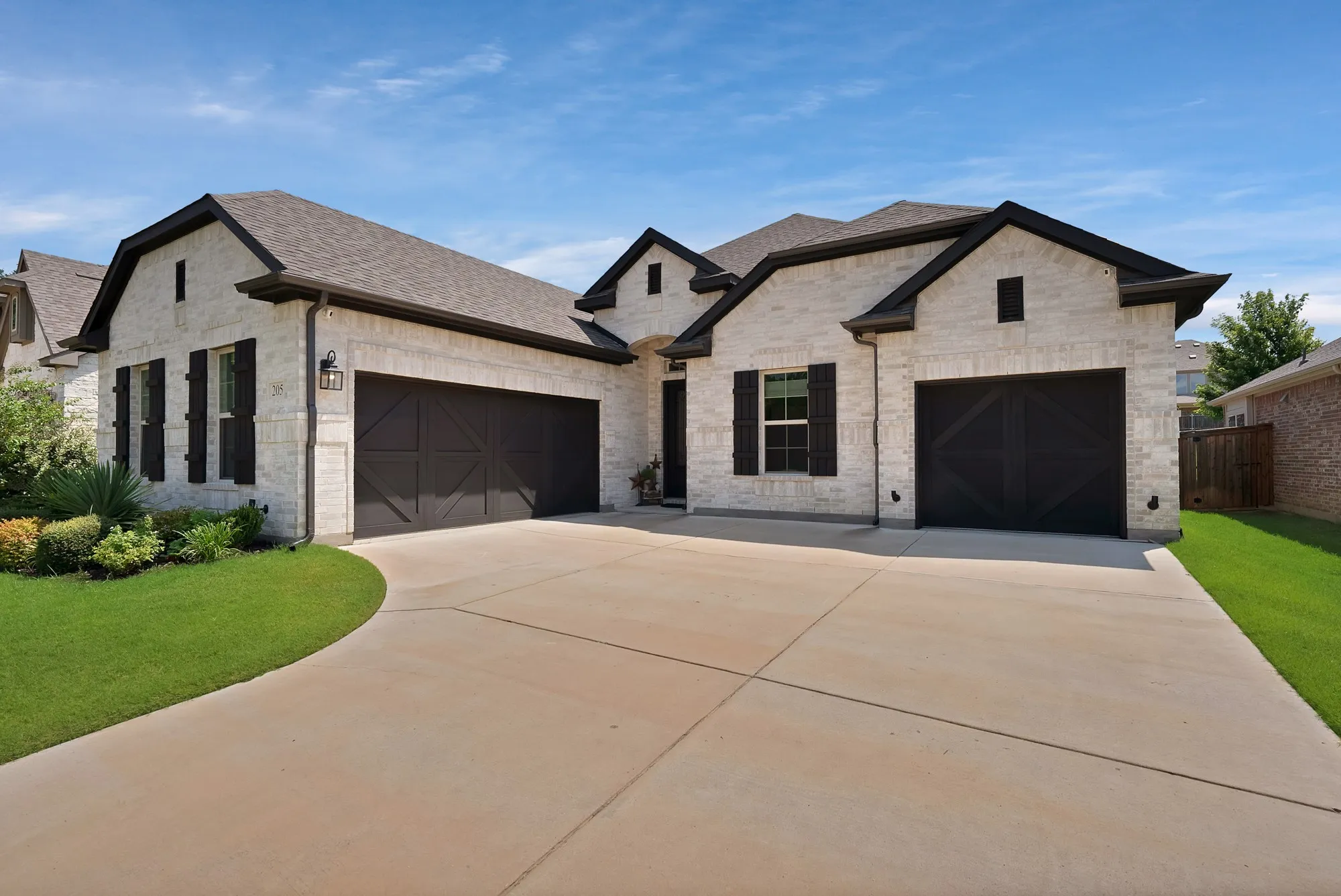 The property features a light-colored brick exterior with dark trim and shutters, complemented by a neatly manicured lawn and a spacious driveway