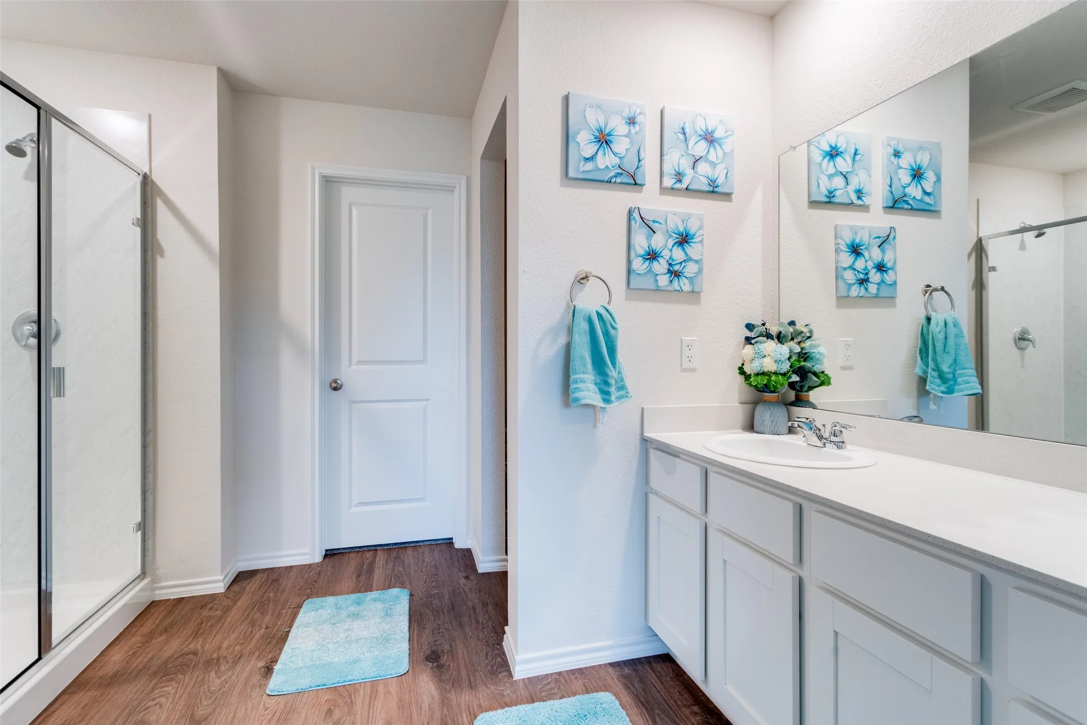 Bathroom featuring wood-finish flooring, a glass-enclosed shower, and a white vanity with an integrated sink and chrome fixtures