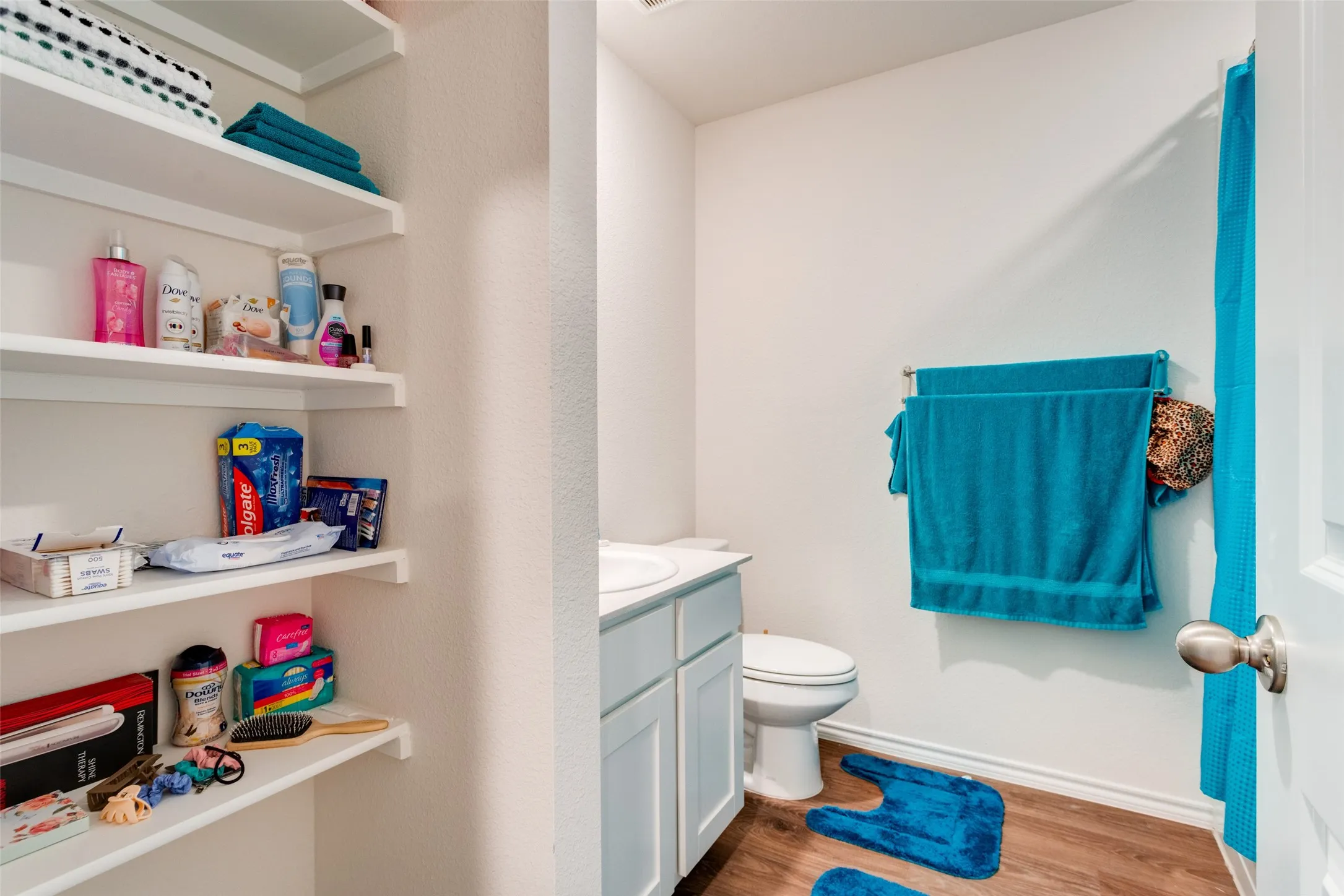 Bathroom featuring a white vanity with an integrated sink, a commode, and wood-finish flooring
