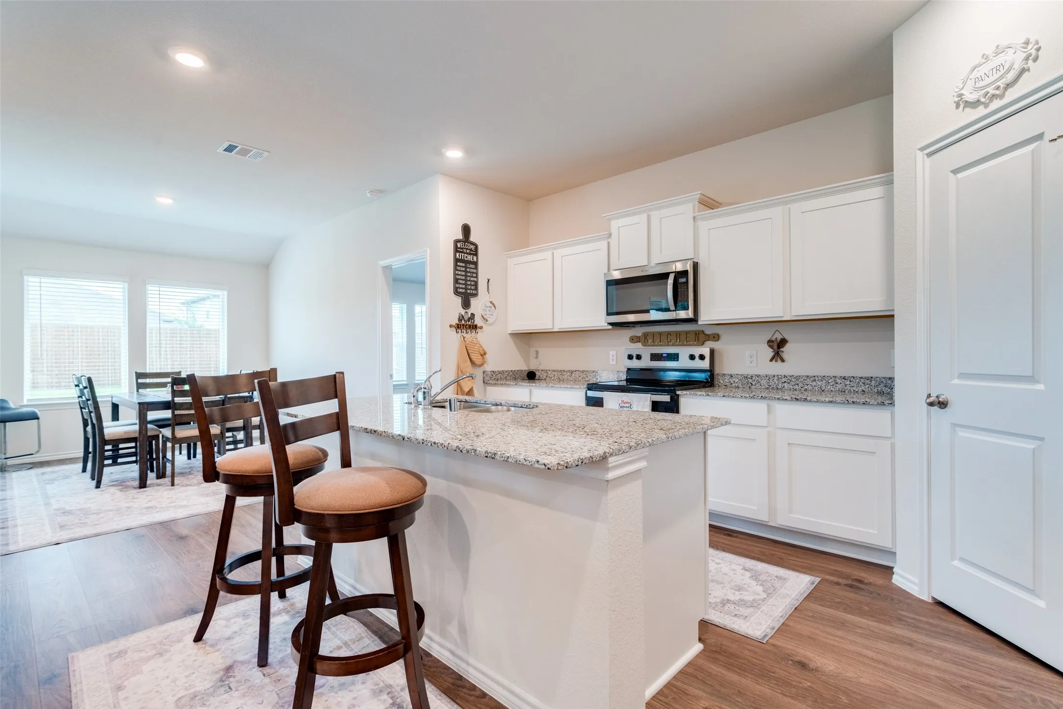 Modern kitchen with a central island featuring a granite countertop, white cabinetry, stainless steel appliances, and wood-finish flooring
