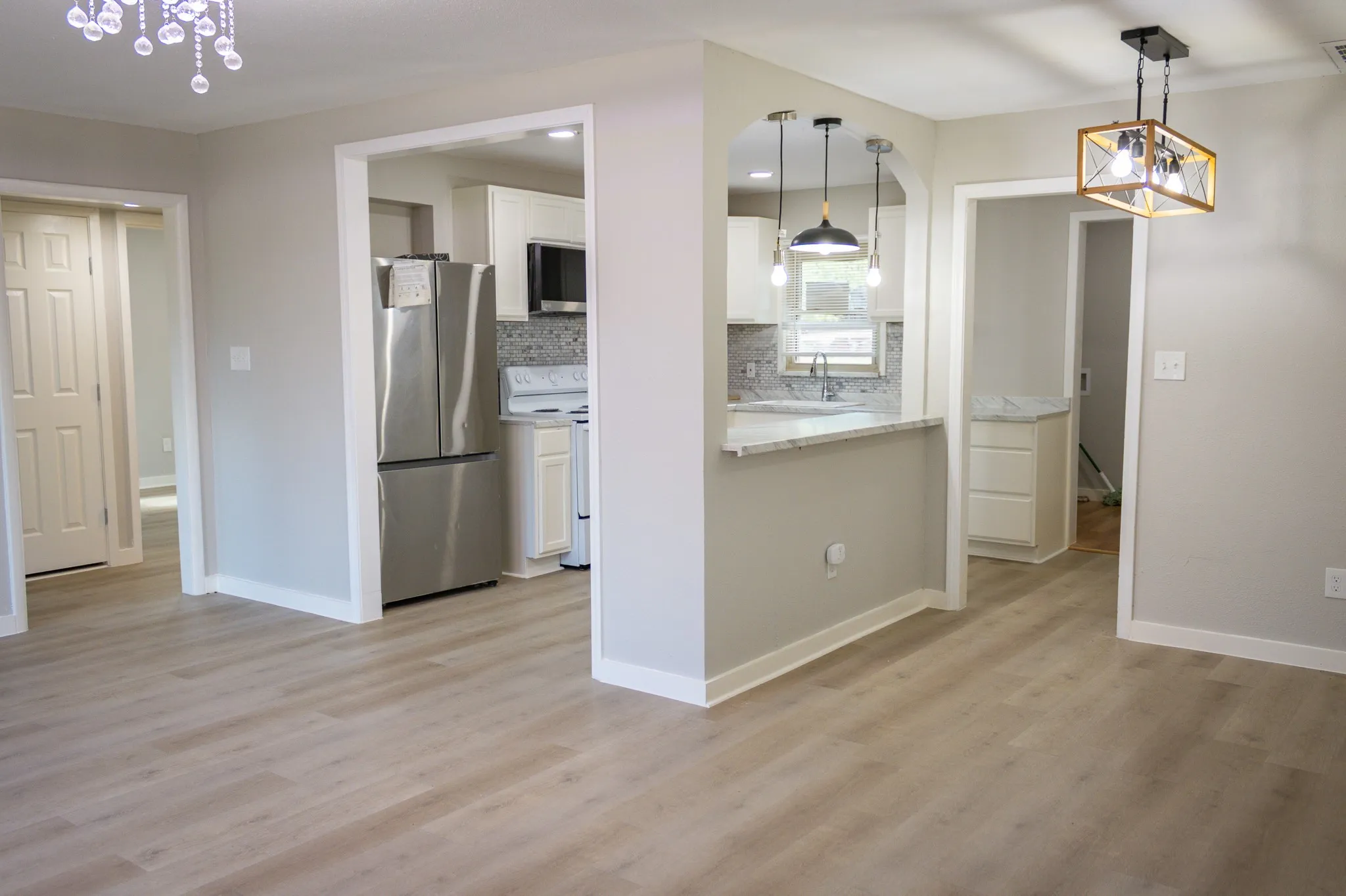 Kitchen with stainless steel appliances, white cabinetry, light wood-type flooring, hanging light fixtures, and tasteful backsplash