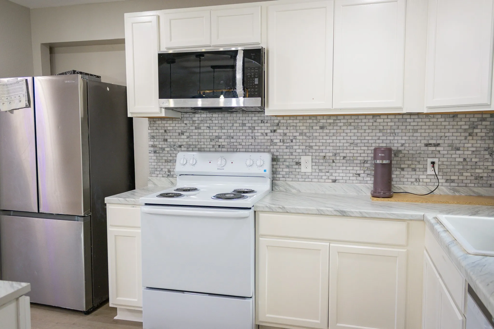 Kitchen featuring stainless steel appliances, backsplash, and white cabinets