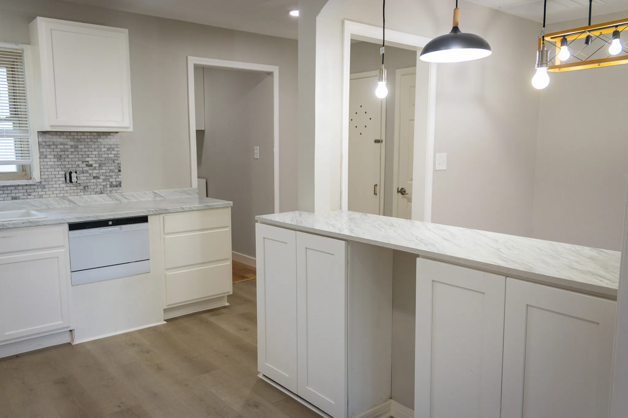 Kitchen featuring white cabinets, light wood-style flooring, backsplash, decorative light fixtures, and light stone counters