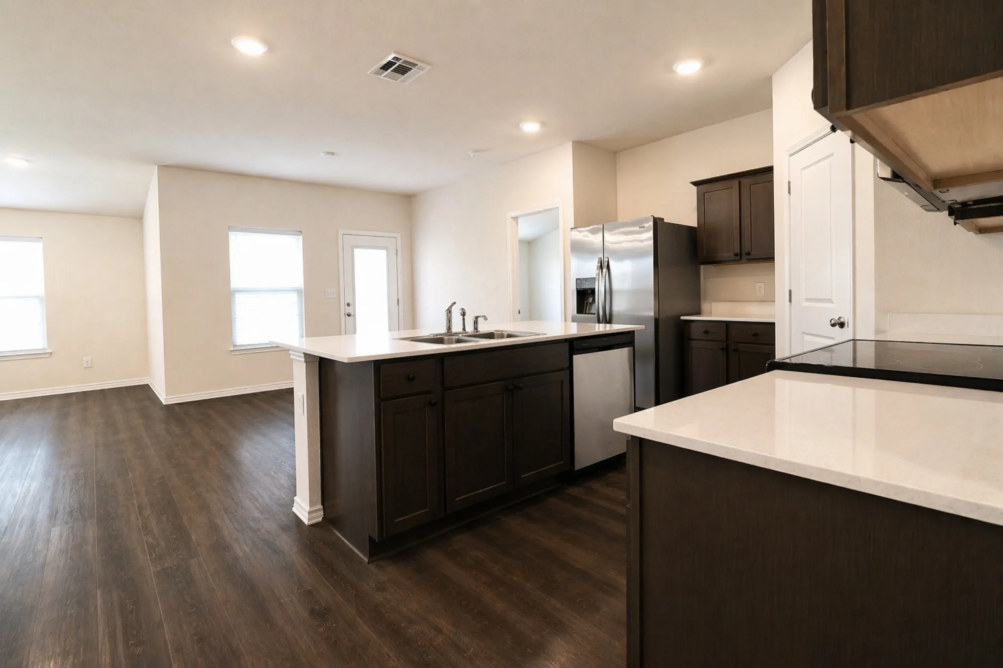 Kitchen featuring a central island with sink, white countertops, dark wood cabinetry, and stainless steel appliances