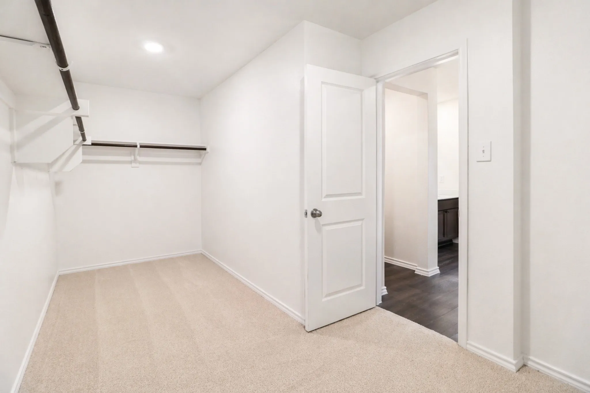 Carpeted room featuring white walls, a white paneled door, and overhead lighting